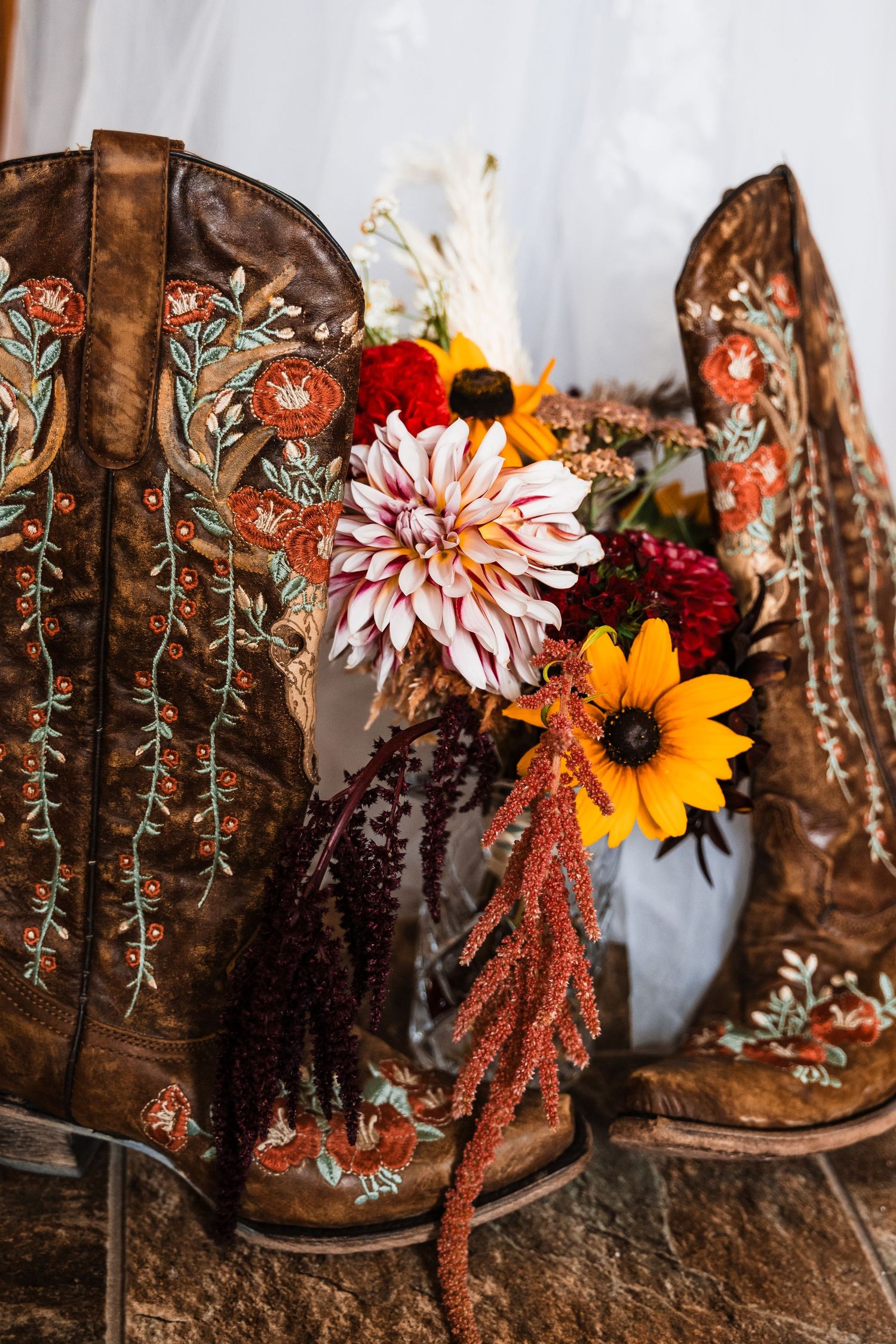 Brown embroidered cowboy boots decorated with flowers featuring sunflowers, dahlias and fall florals in rustic setting.