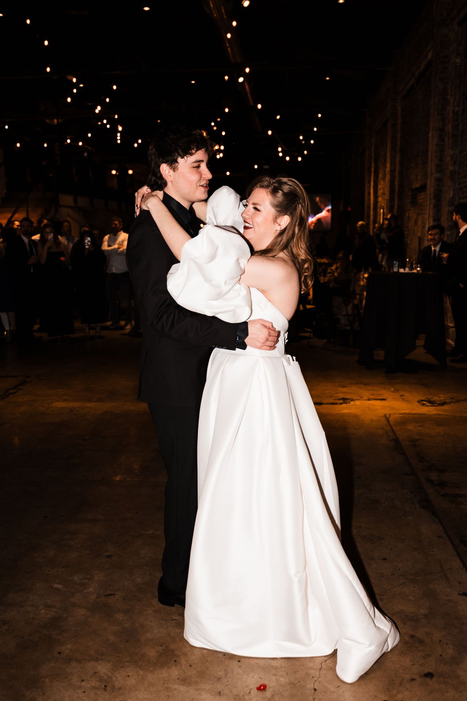 A couple shares a happy dance moment under twinkling lights at their wedding reception.