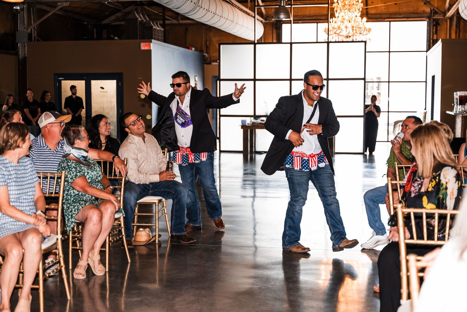 Entertainers perform during an event at a modern venue with floor-to-ceiling windows and guests seated in gold chairs.