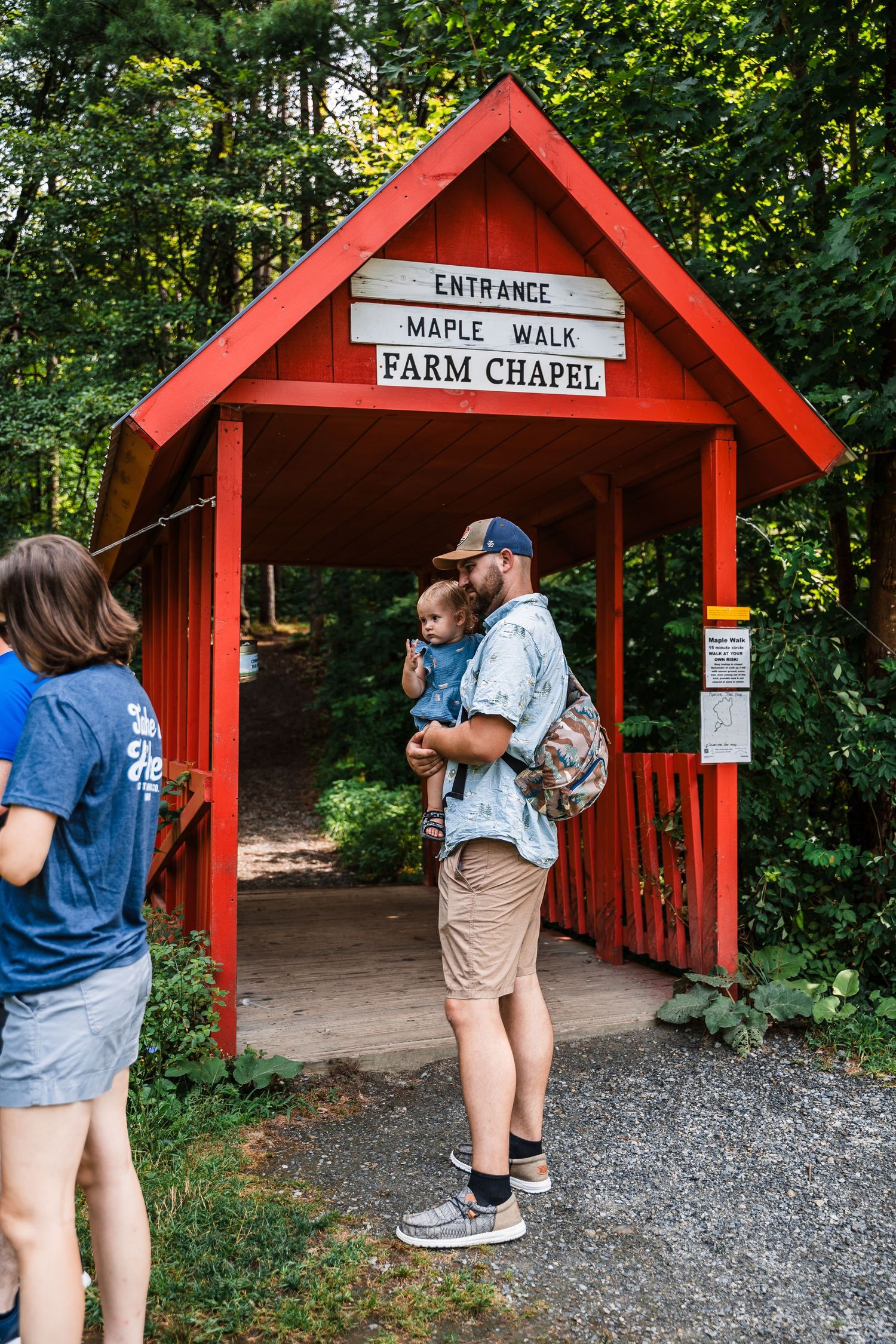 Visitors stand at the entrance of a red Farm Chapel covered bridge with rustic signage.