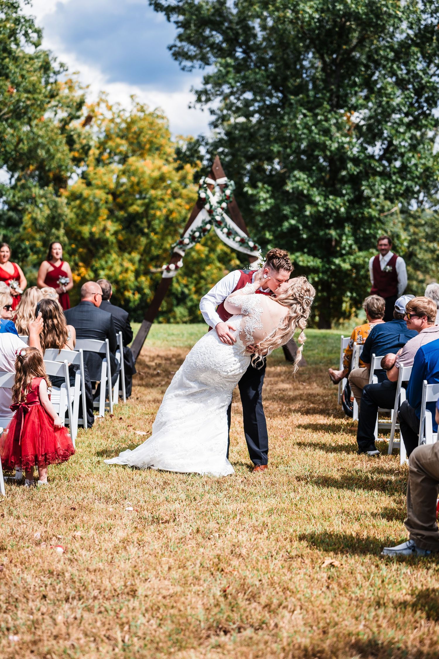 A couple shares a dramatic dip kiss during their outdoor wedding ceremony as guests look on.