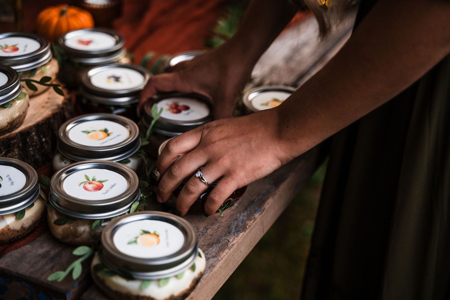 Hands arranging decorated mason jars on a wooden surface at an outdoor event.