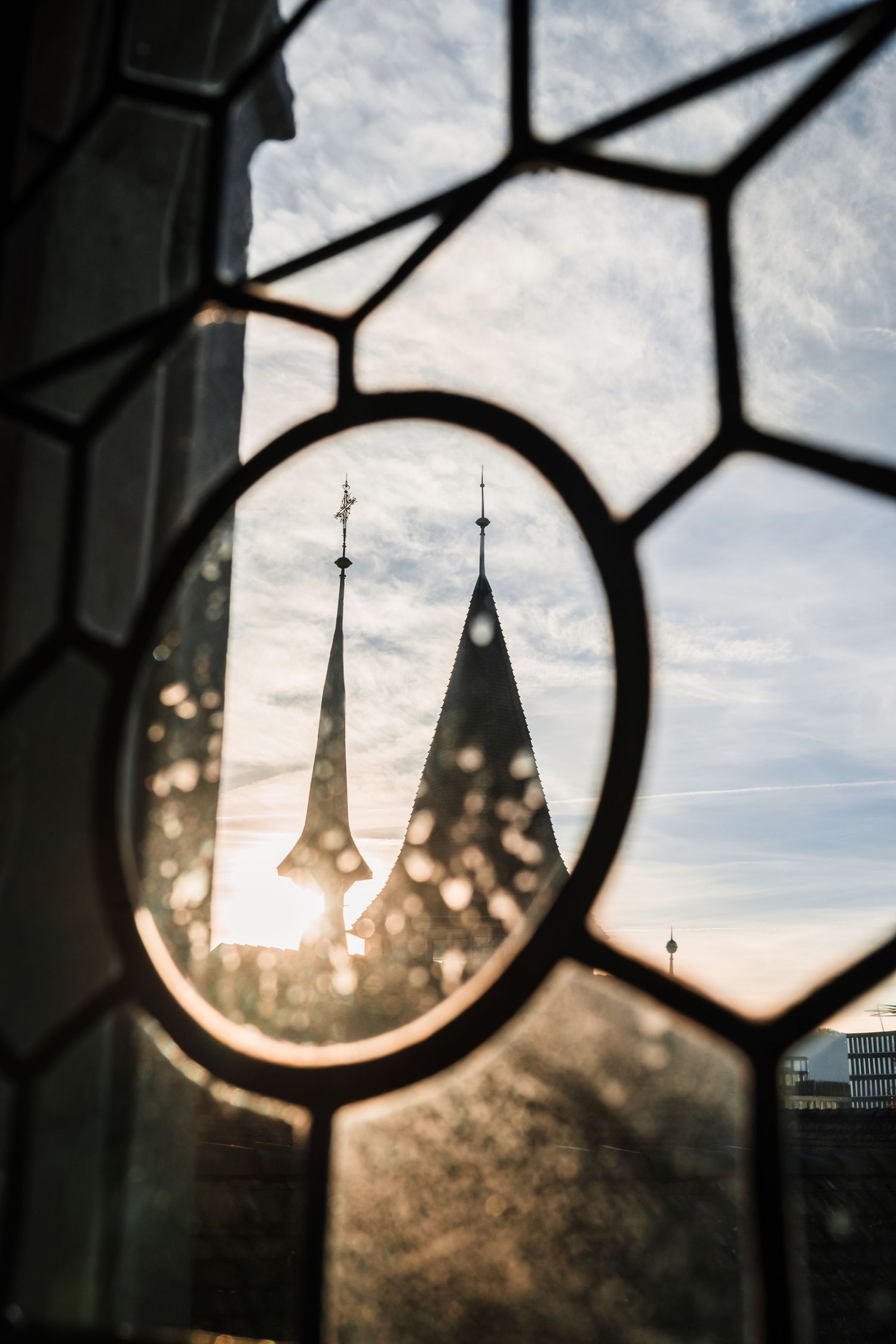 Church spires silhouetted against cloudy sky seen through geometric stained glass window patterns.