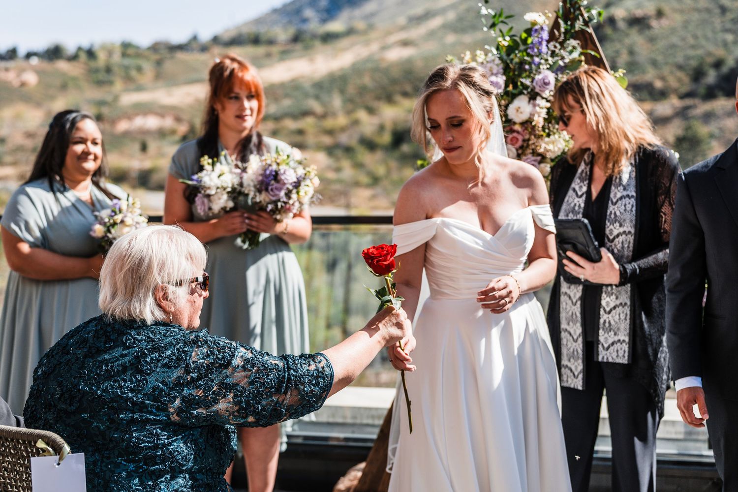 Guest presenting a red rose to the bride during an outdoor mountain wedding ceremony.
