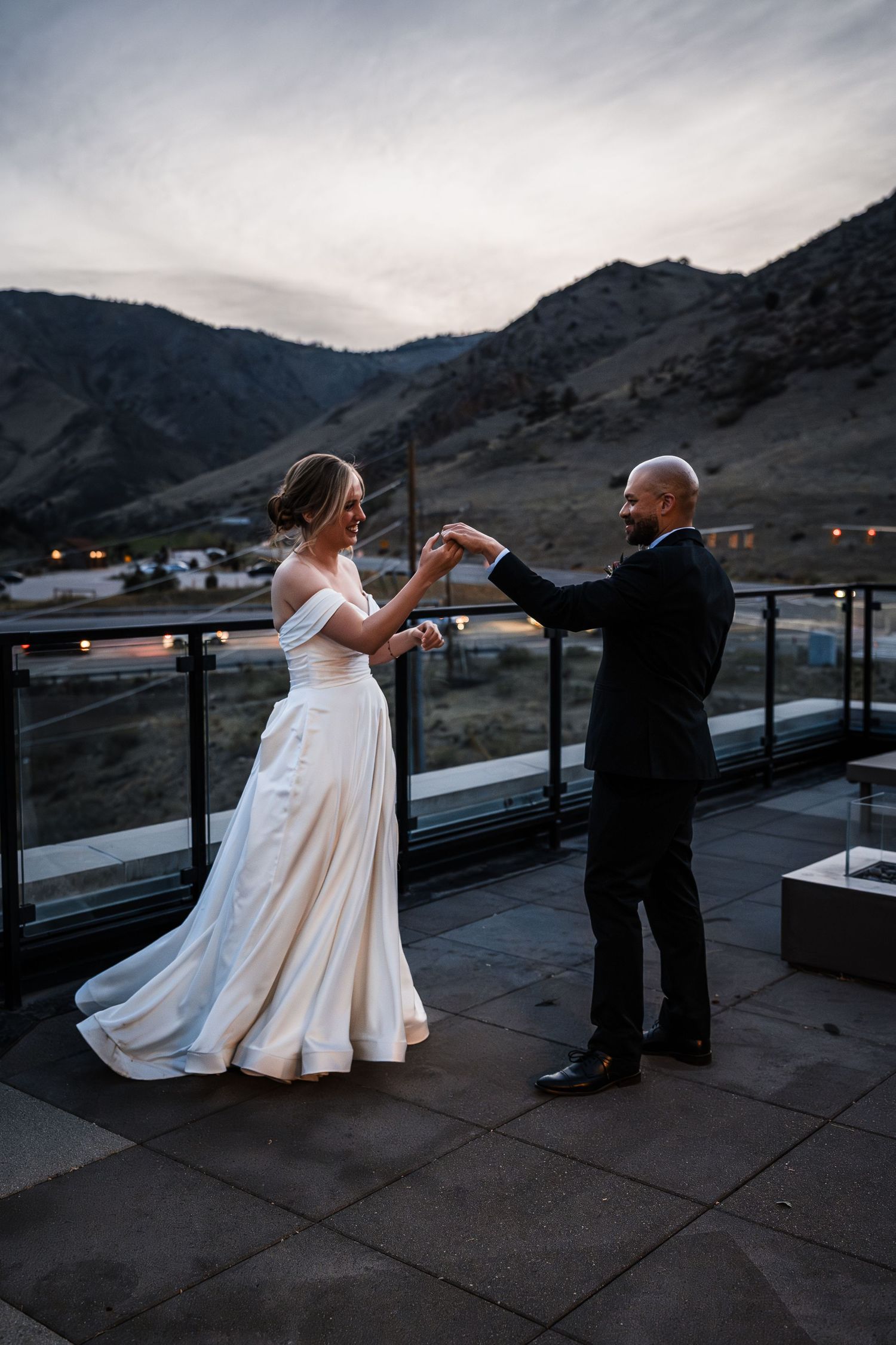 Bride and groom sharing first dance on rooftop terrace with mountain backdrop at dusk.
