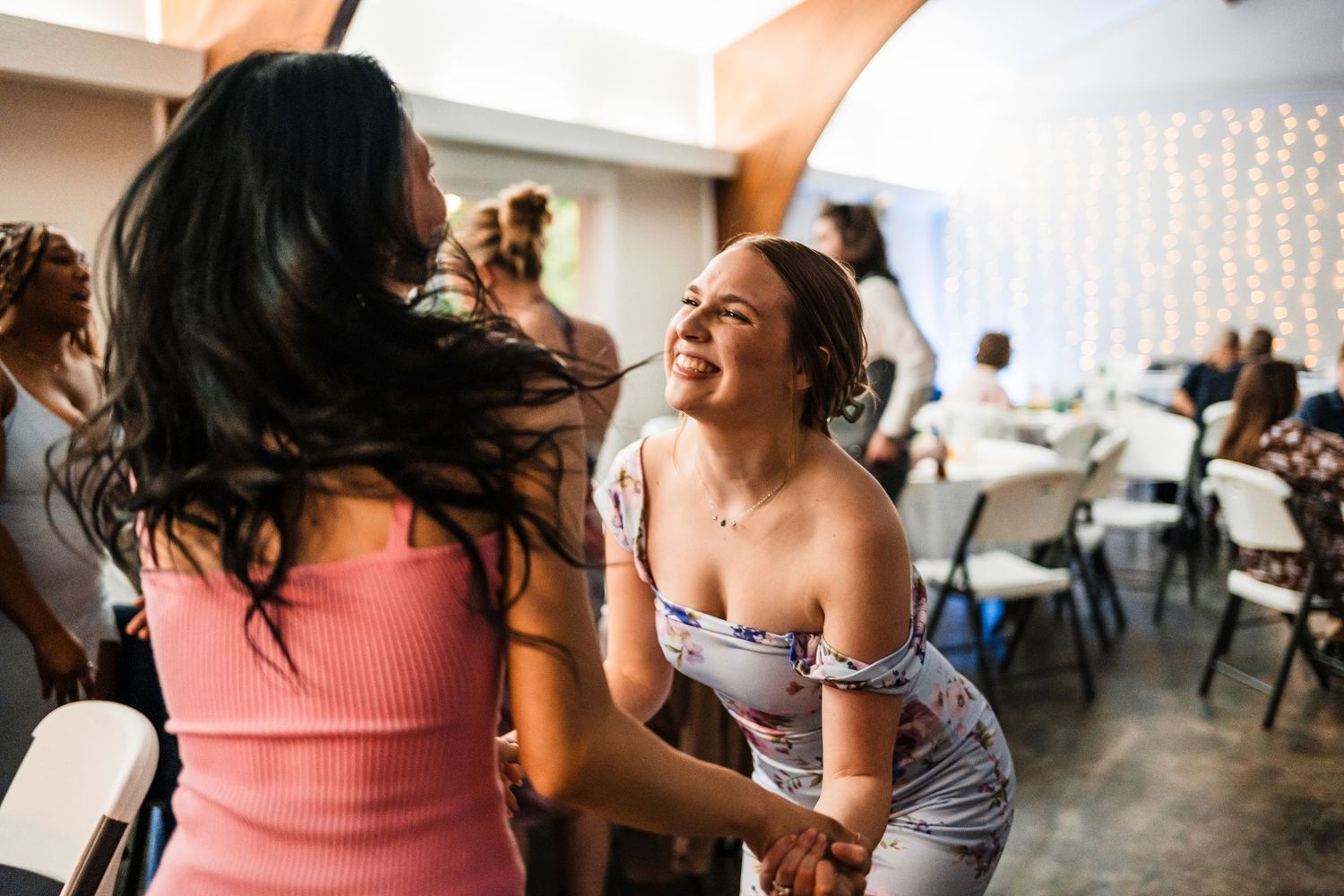 Two women laughing and dancing together at a joyful wedding celebration.
