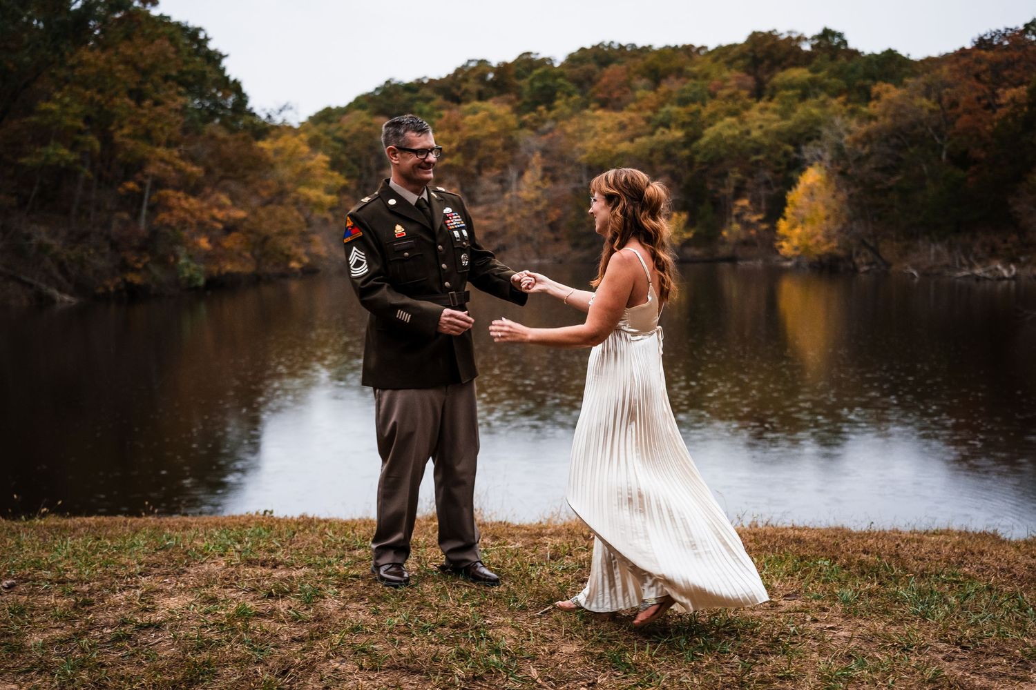 Couple posing for romantic photos by a lake surrounded by fall colors.