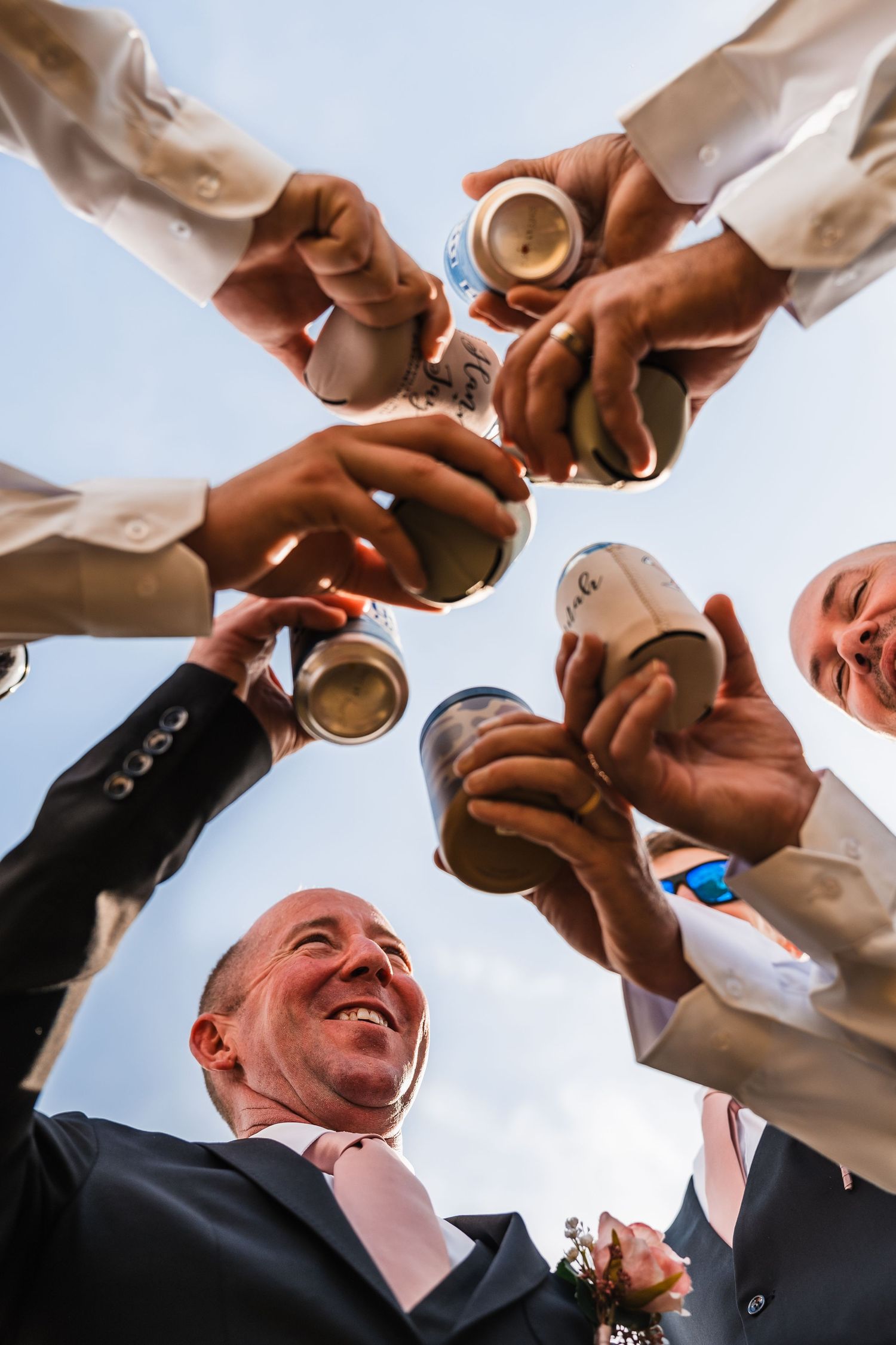 Low angle view of people toasting with drinks against a bright sky during a celebration.