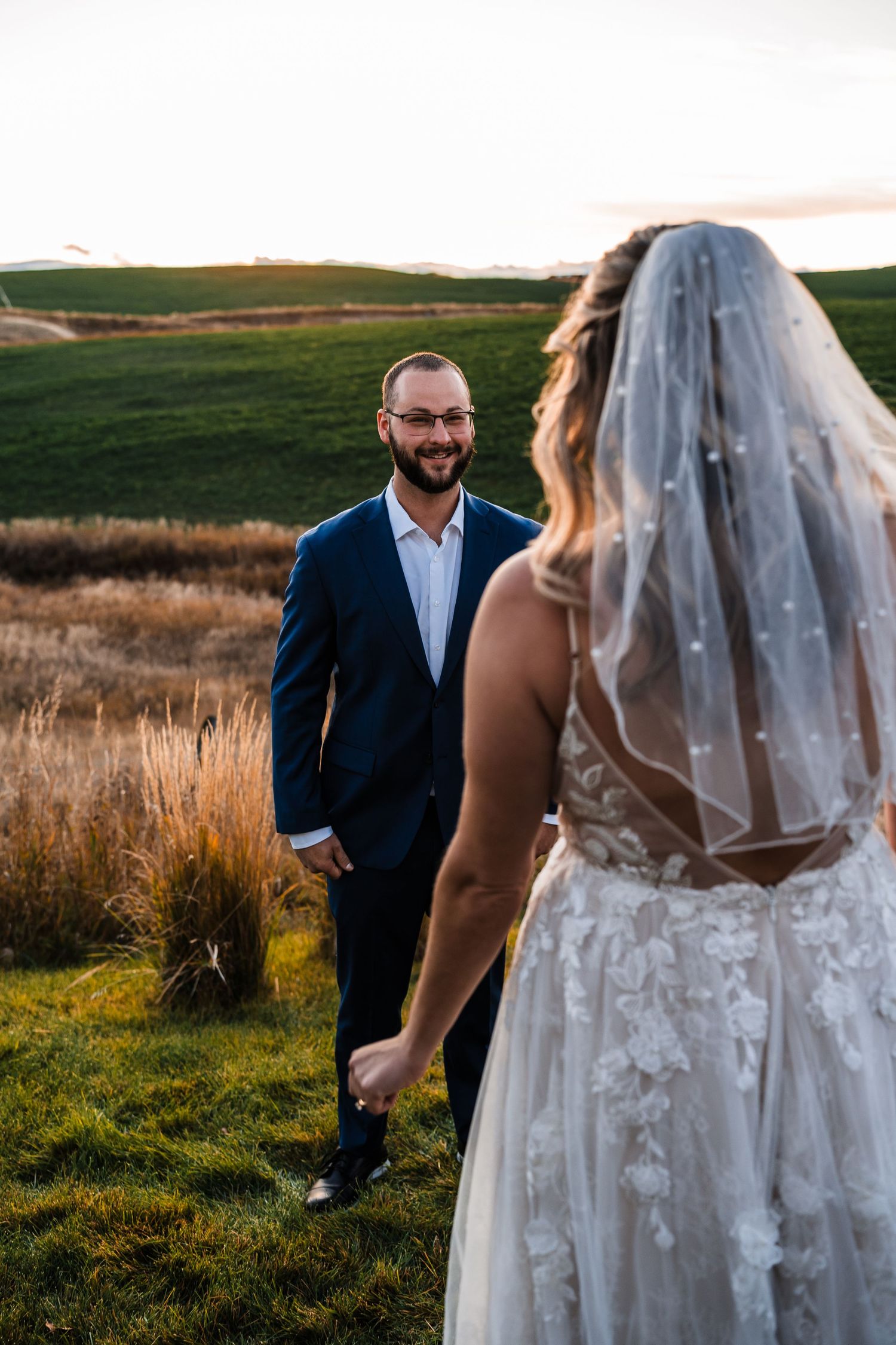 A couple shares a romantic moment in a grassy field during their wedding photoshoot at sunset.