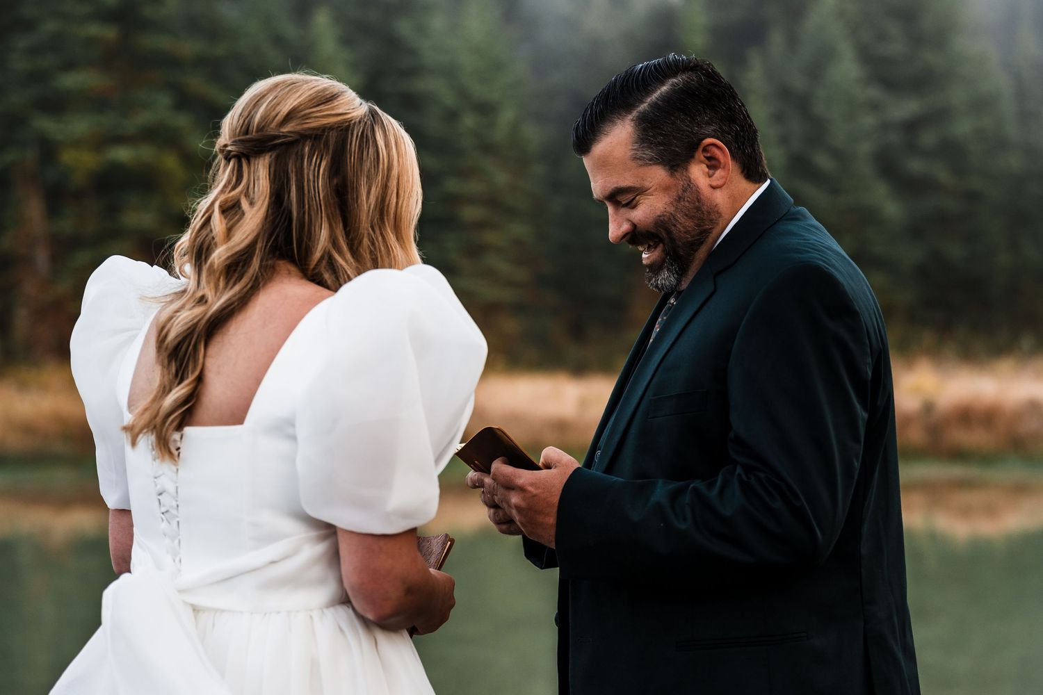 A couple shares emotional moments while reading handwritten vows by a serene lake.