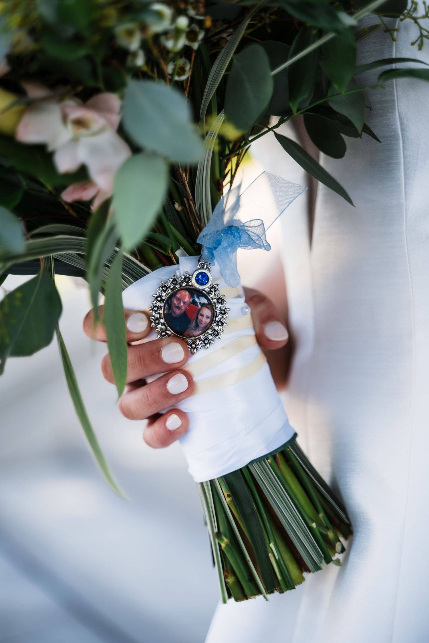 Wedding bouquet wrapped in white ribbon with blue accent and vintage brooch detail.