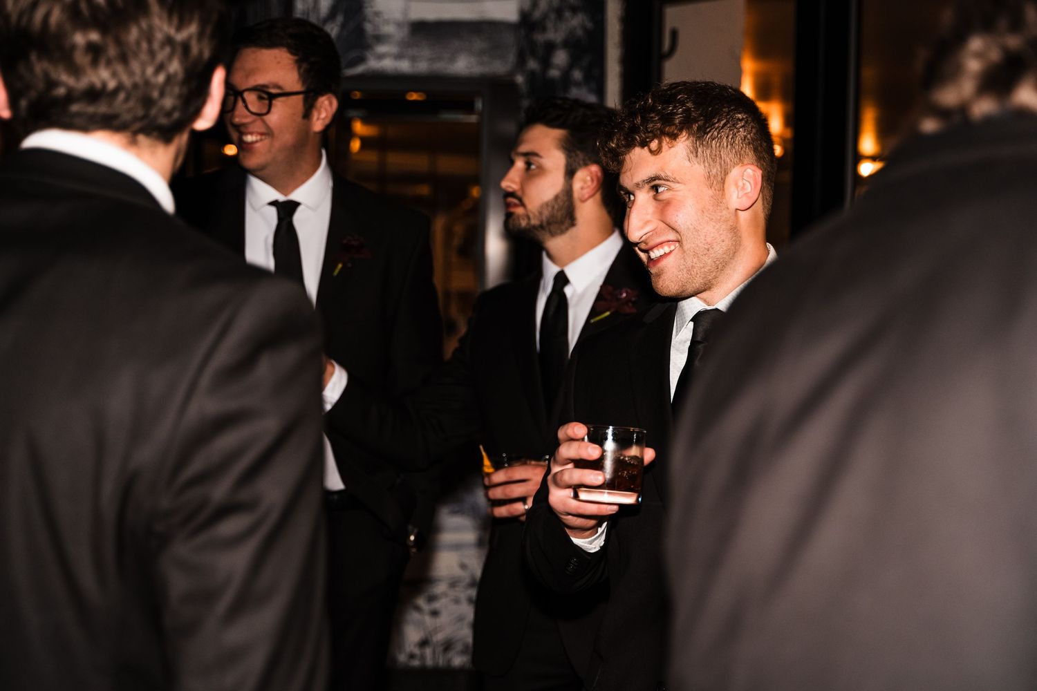 Group of guests in formal attire socializing at evening wedding reception.