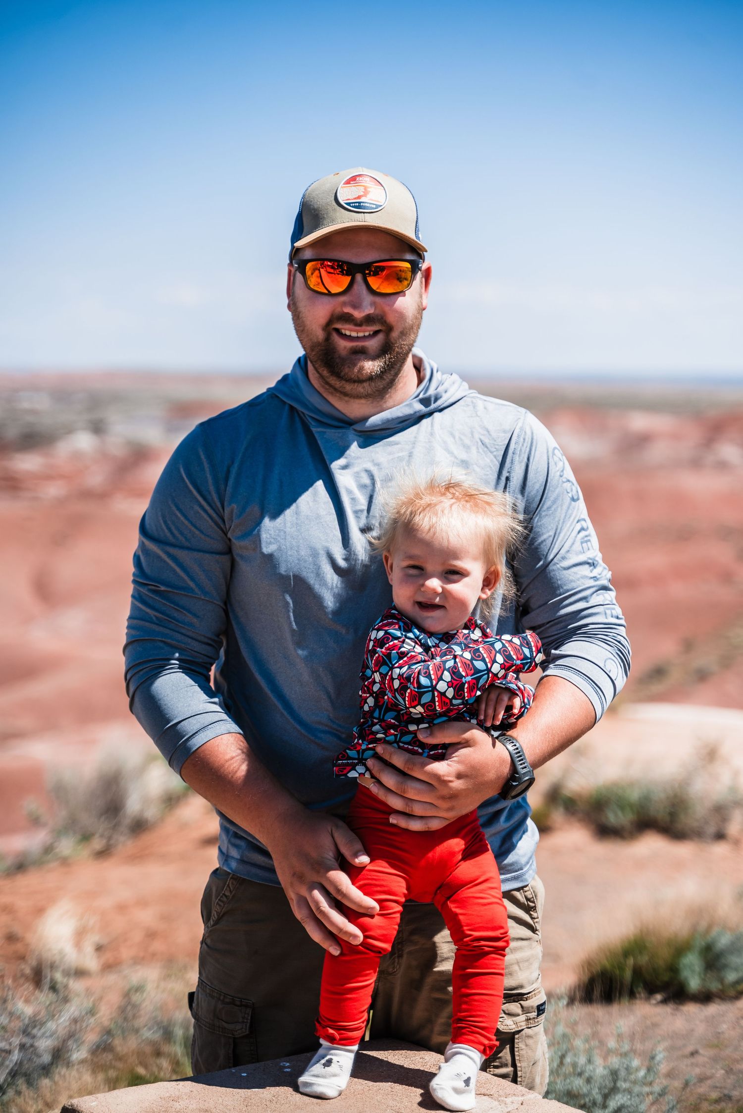 Adult and small child enjoy scenic overlook of red desert landscape.