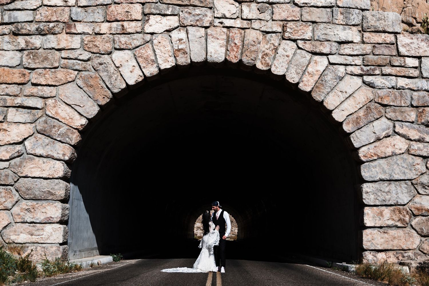 Silhouetted figures in a stone tunnel creating dramatic wedding photograph.