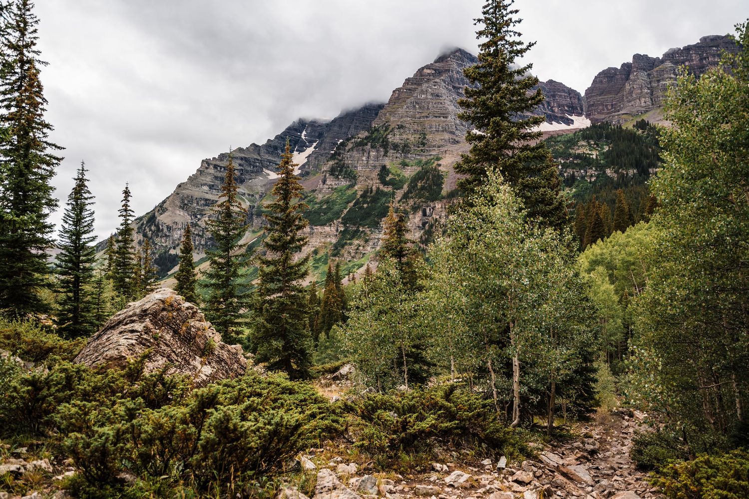 Majestic mountain range with jagged peaks and patches of snow towers above alpine forest.