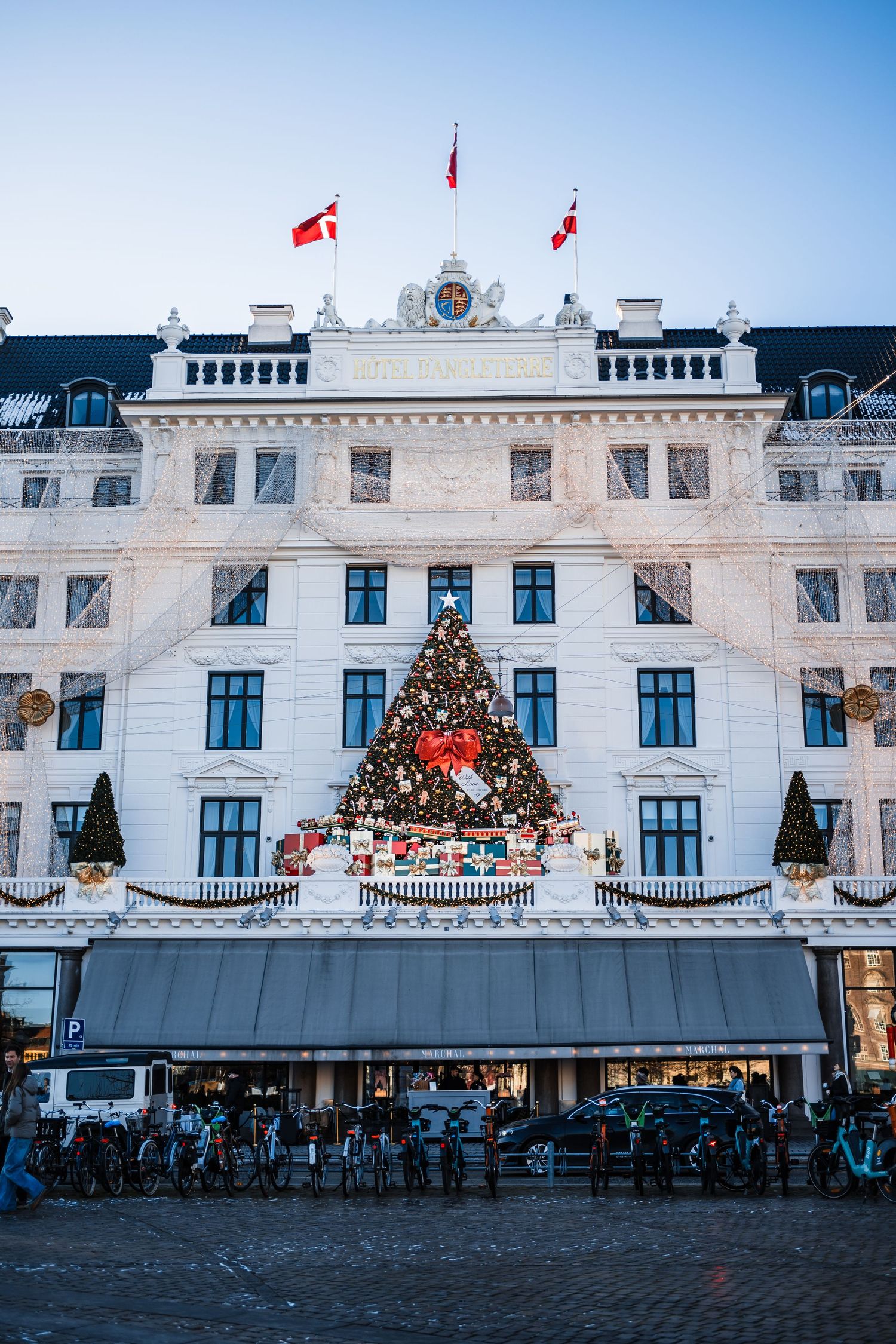 White ornate hotel buildings decorated with Christmas garlands and flags line a town square in Denmark.