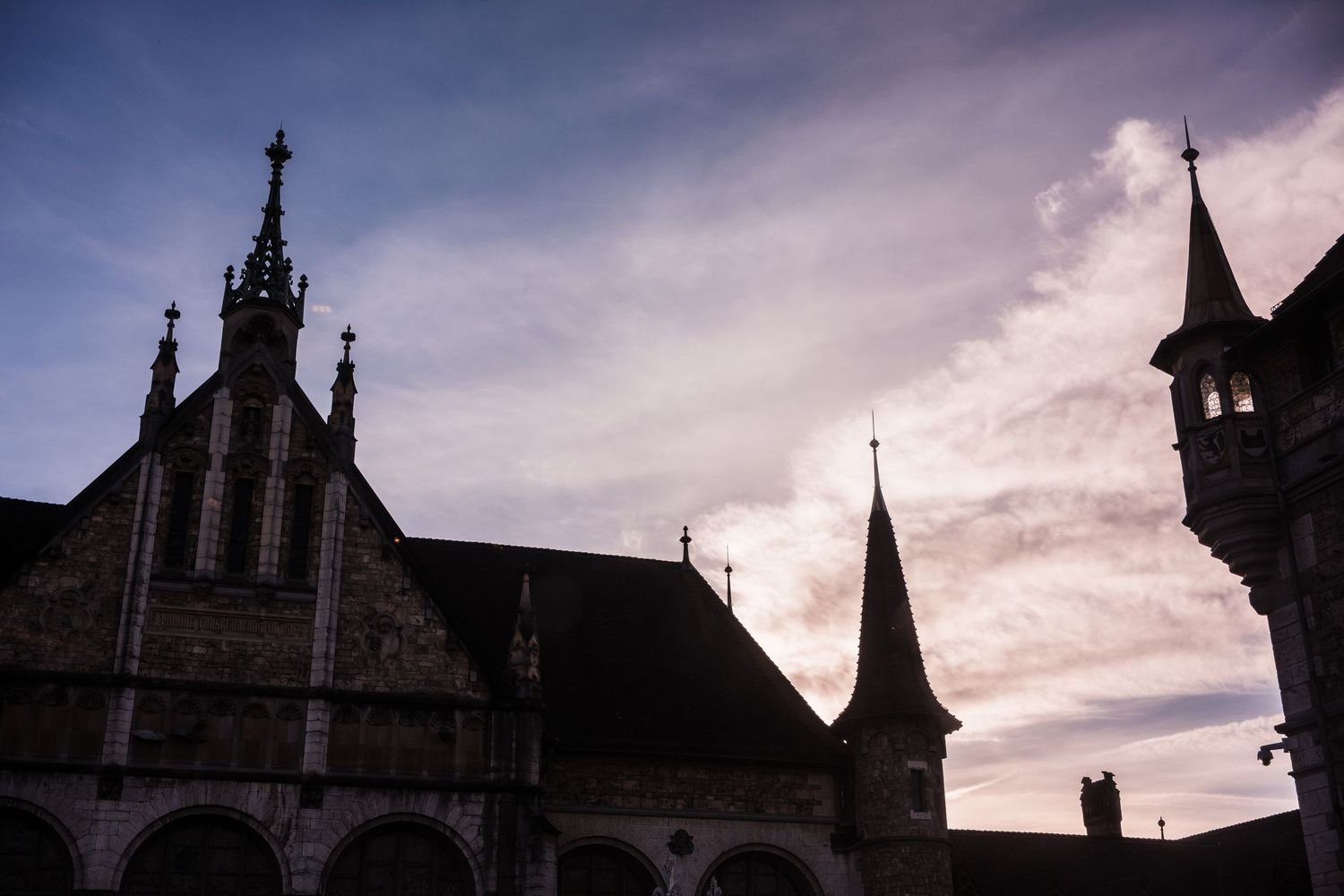 Gothic church spires and towers silhouetted against dramatic cloudy sky at sunset create a moody architectural scene.