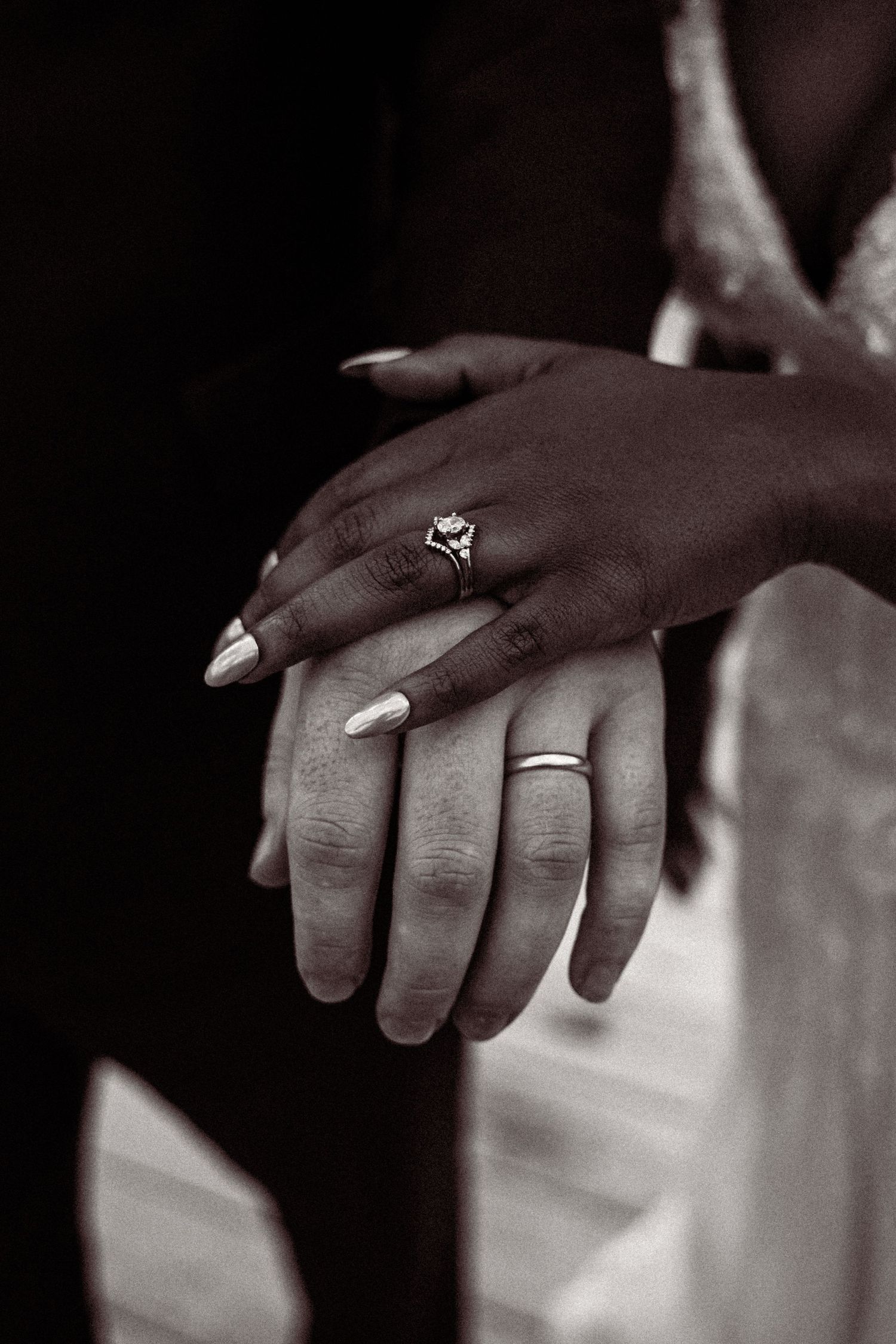 Black and white close-up of newlyweds hands showing diamond engagement ring and wedding band.