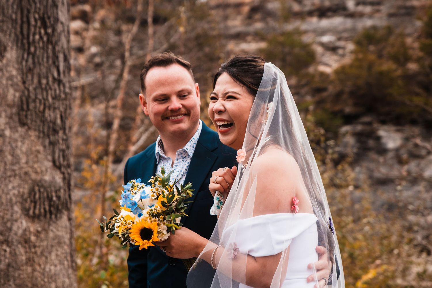 Joyful candid moment between couple with sunflower bouquet during outdoor fall wedding.