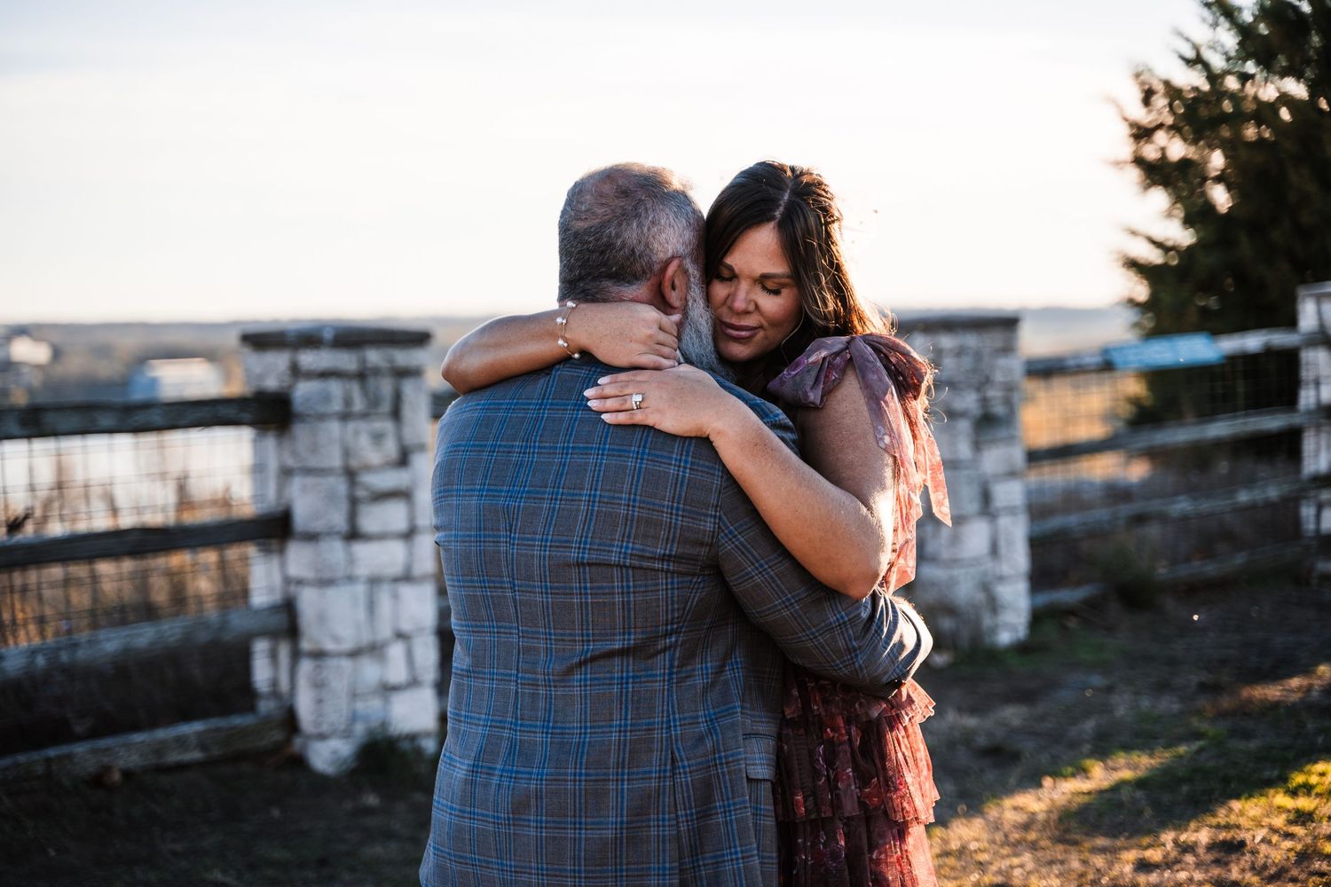 A couple embraces in warm sunset light against a stone wall backdrop.