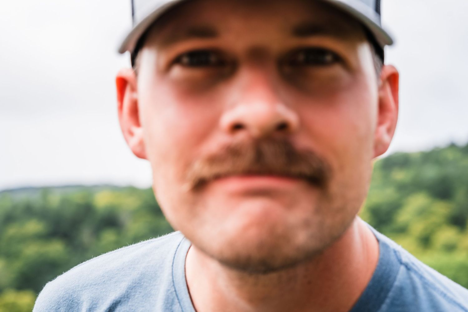 A close-up view of someone wearing a baseball cap outdoors with hills in the background.