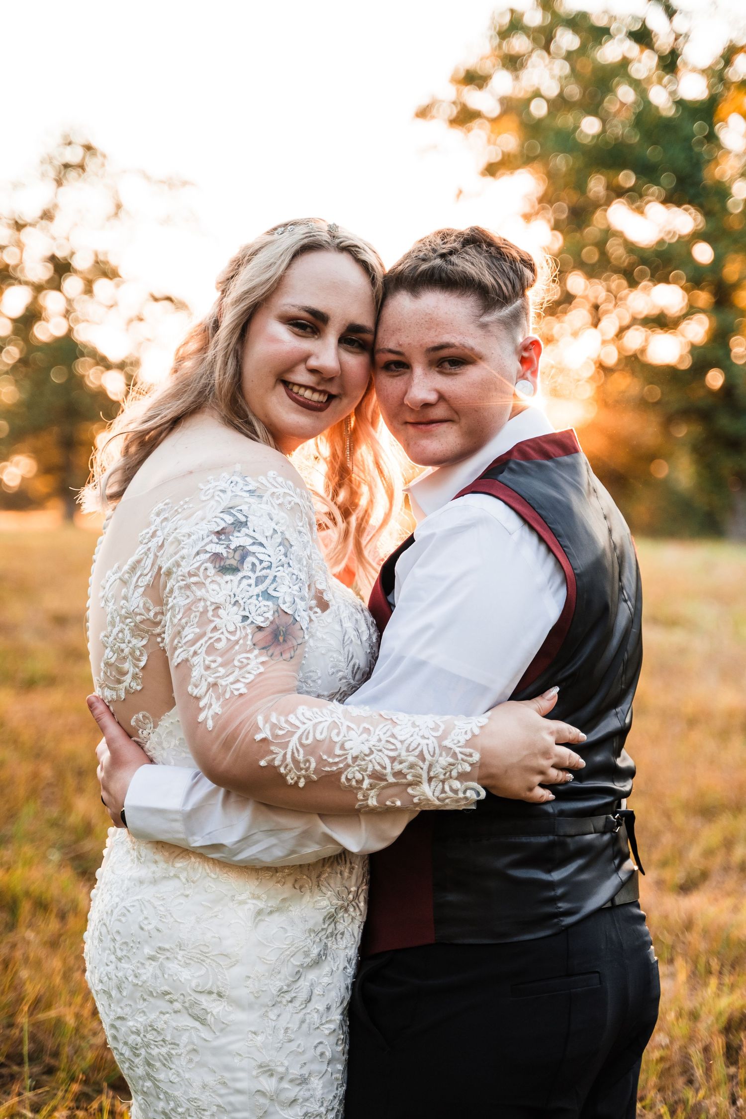 A romantic sunset outdoor wedding portrait showing two newlyweds embracing in a golden field.