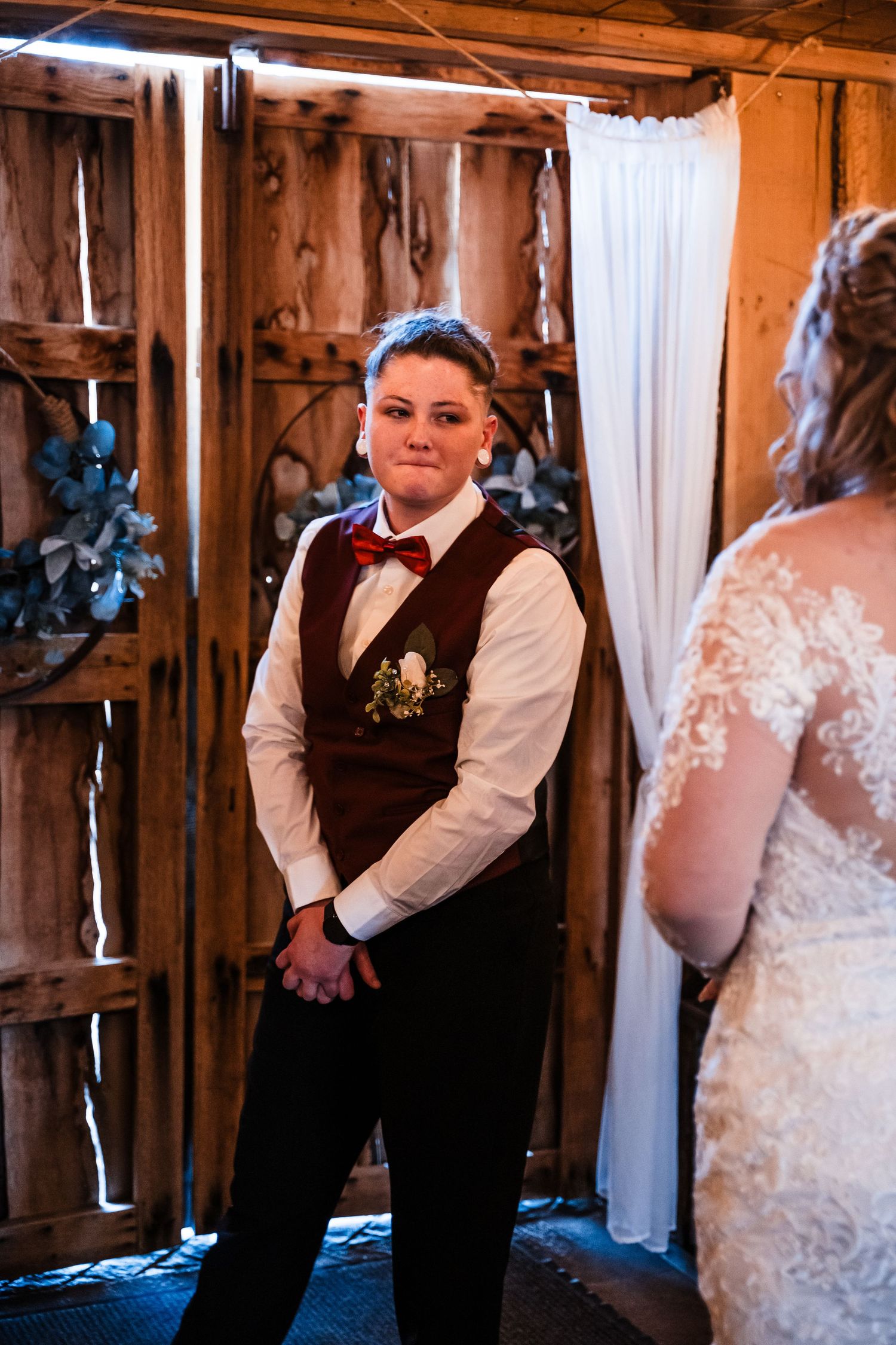 Wedding ceremony in rustic wooden barn interior with white draping and vintage decor.