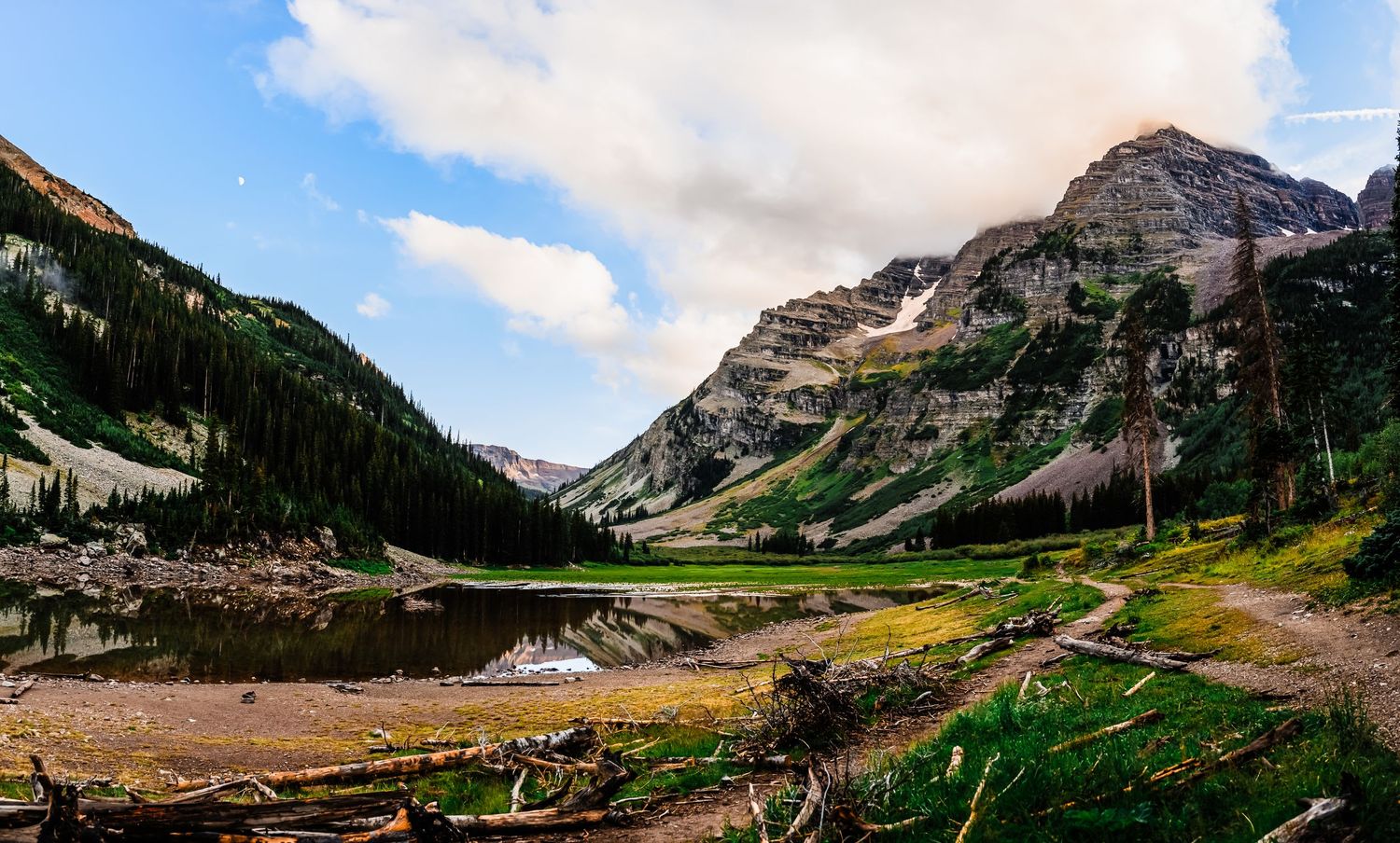 Scenic mountain landscape with a pristine alpine lake surrounded by towering peaks and forested slopes in the wilderness.