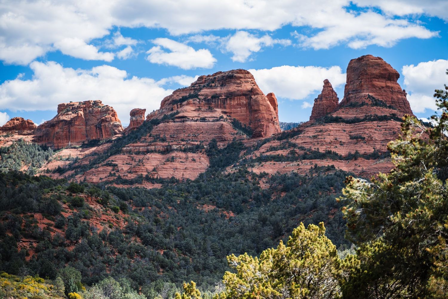 Red sandstone rock formations rise against blue skies in Sedona, Arizona's desert landscape.