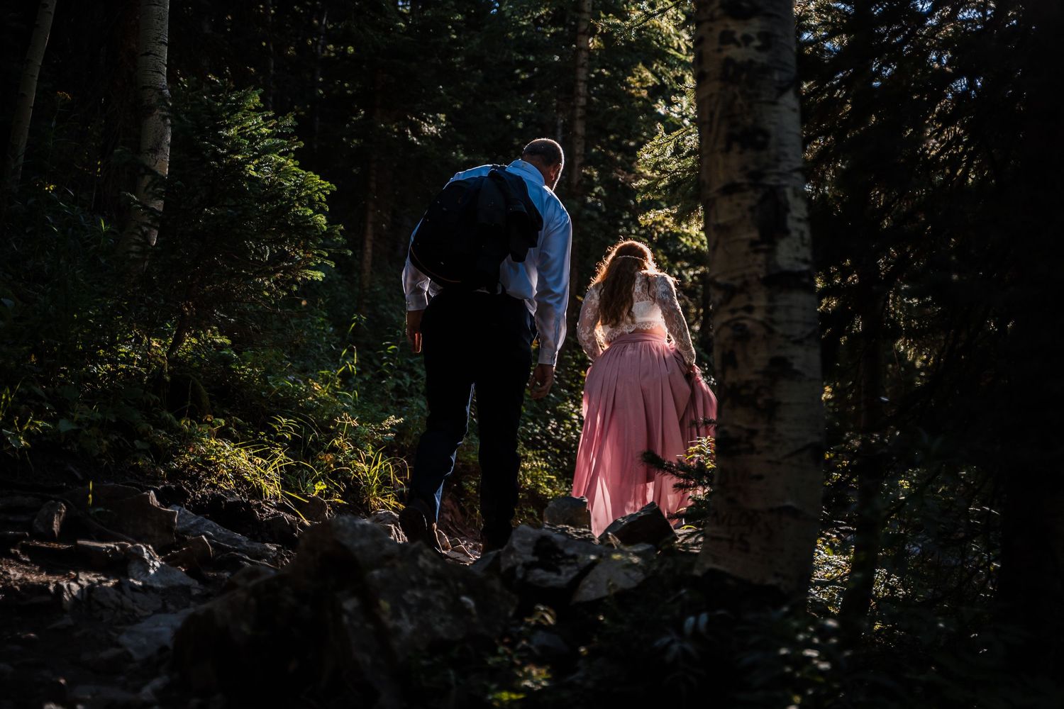 A couple walks through a magical forest path with sunlight filtering through the trees.