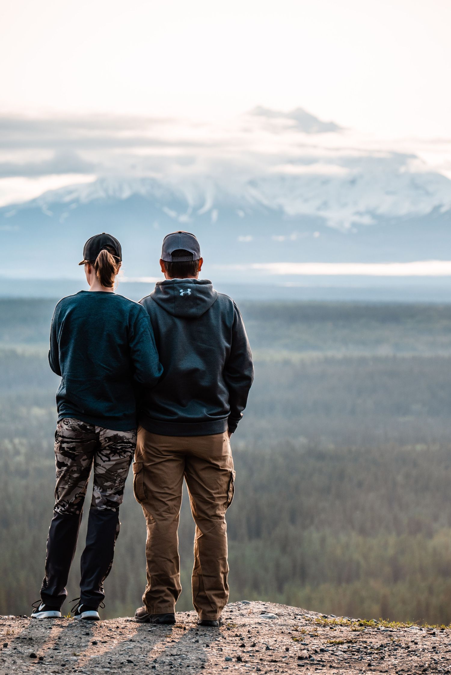 Two people stand together overlooking a misty mountain valley at sunset.
