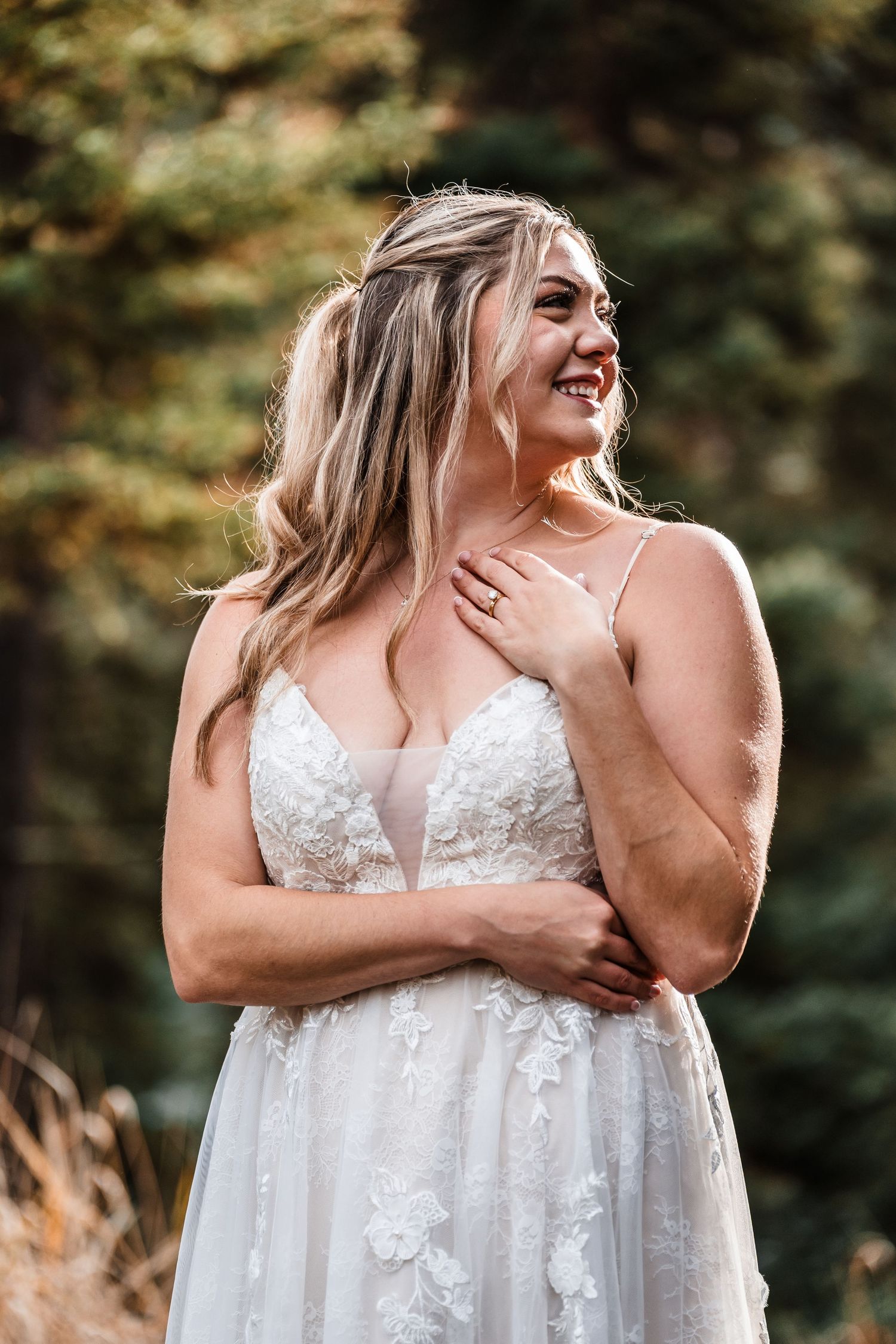 A joyful bride in a lace wedding dress laughs during an outdoor portrait session.
