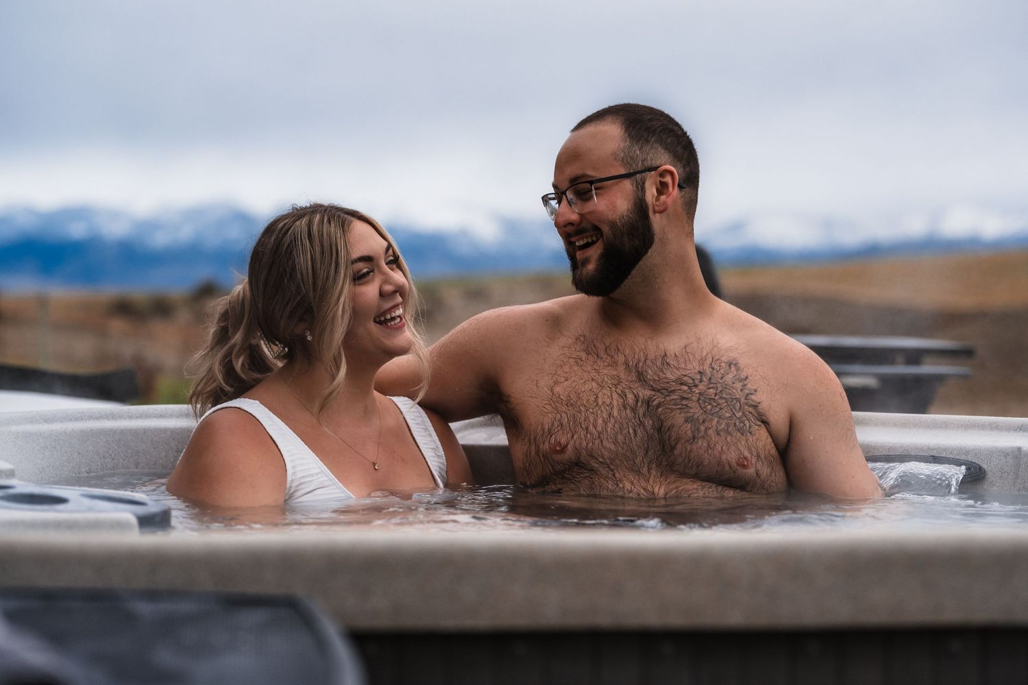 Couple enjoying a relaxing soak in an outdoor hot tub with scenic mountain views in the background.