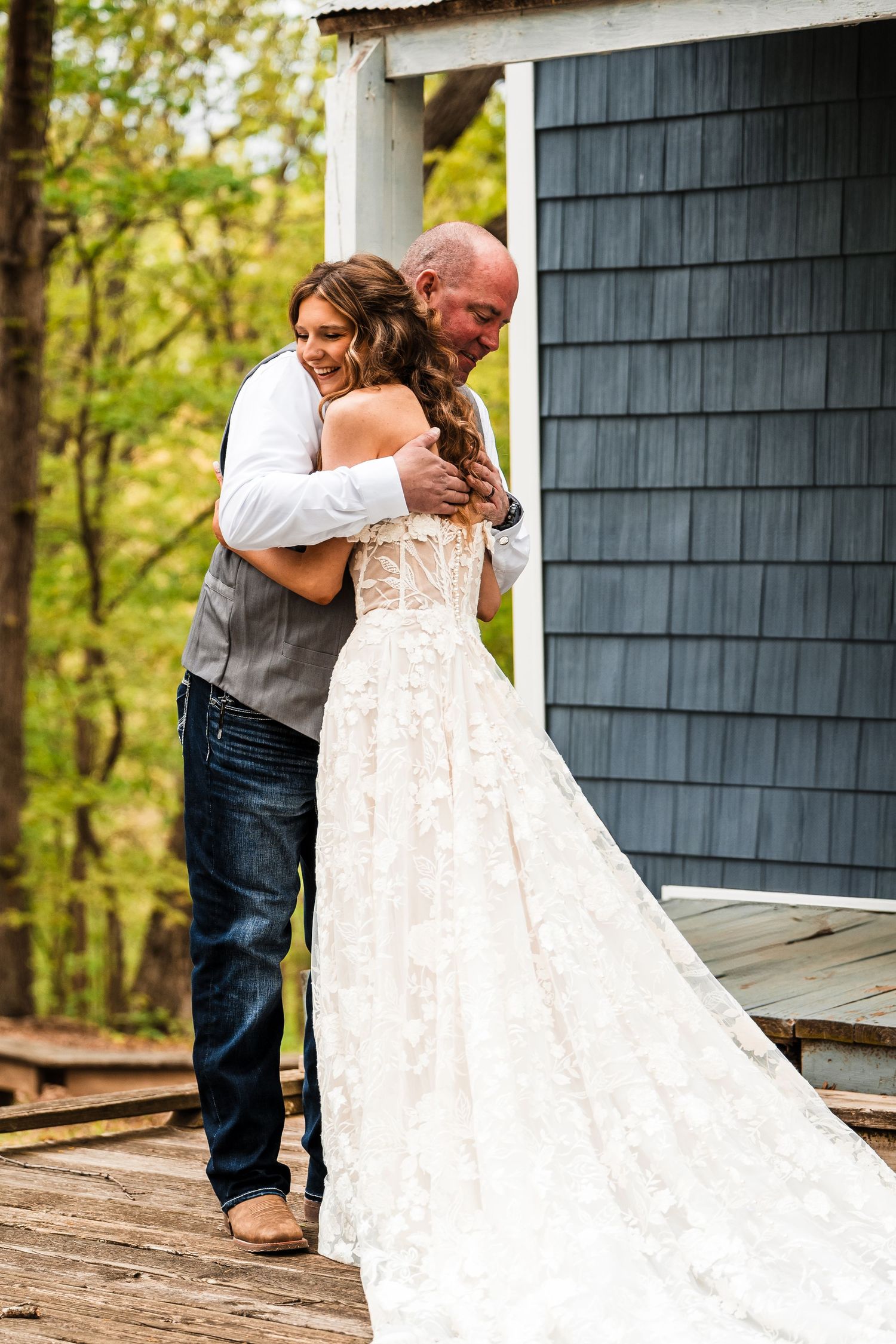 A tender moment between a couple in wedding attire on a rustic wooden porch with grey siding.