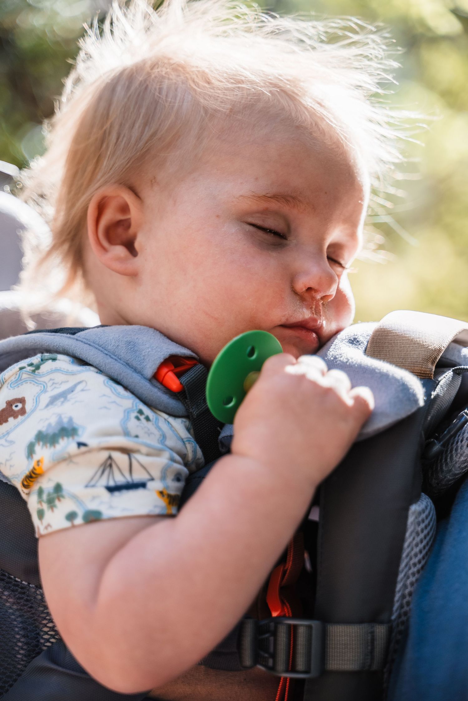 Sleeping toddler in carrier with pacifier during outdoor adventure.