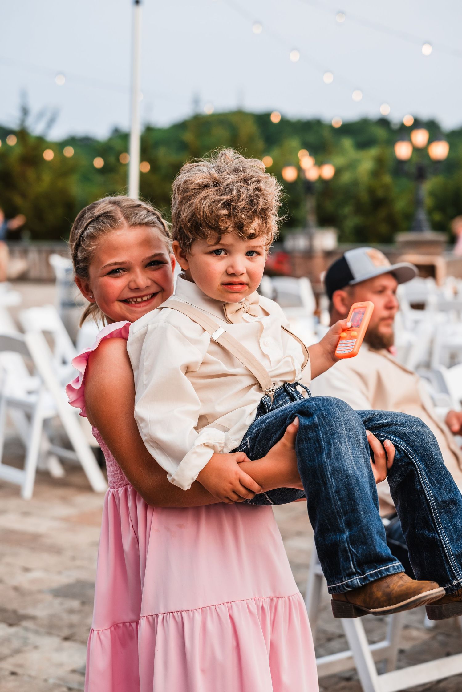 Children in pink and white outfits playing and laughing during outdoor wedding festivities.