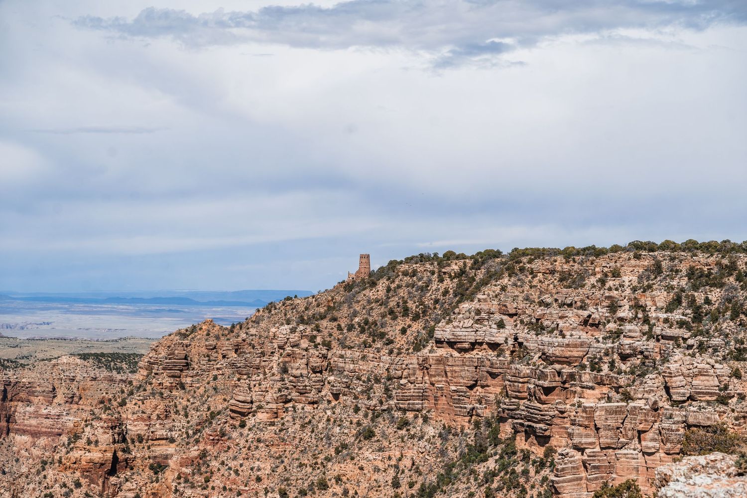 Desert cliffs and rock formations stretch across the rugged landscape under cloudy skies.