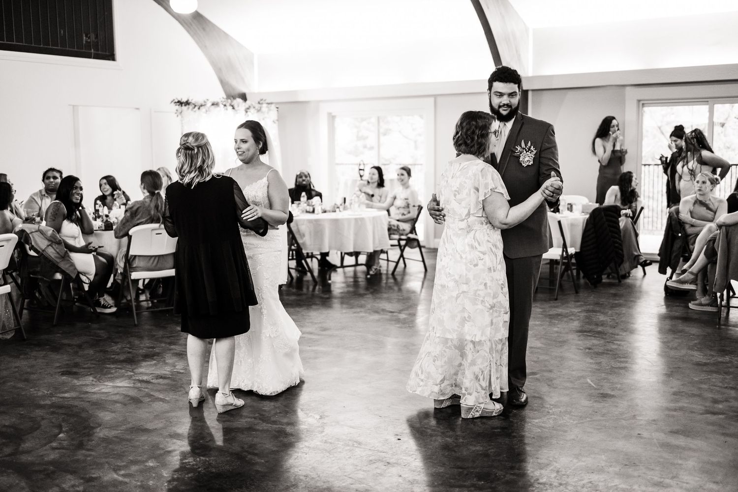 Black and white photo of couples dancing at wedding reception in an indoor venue.