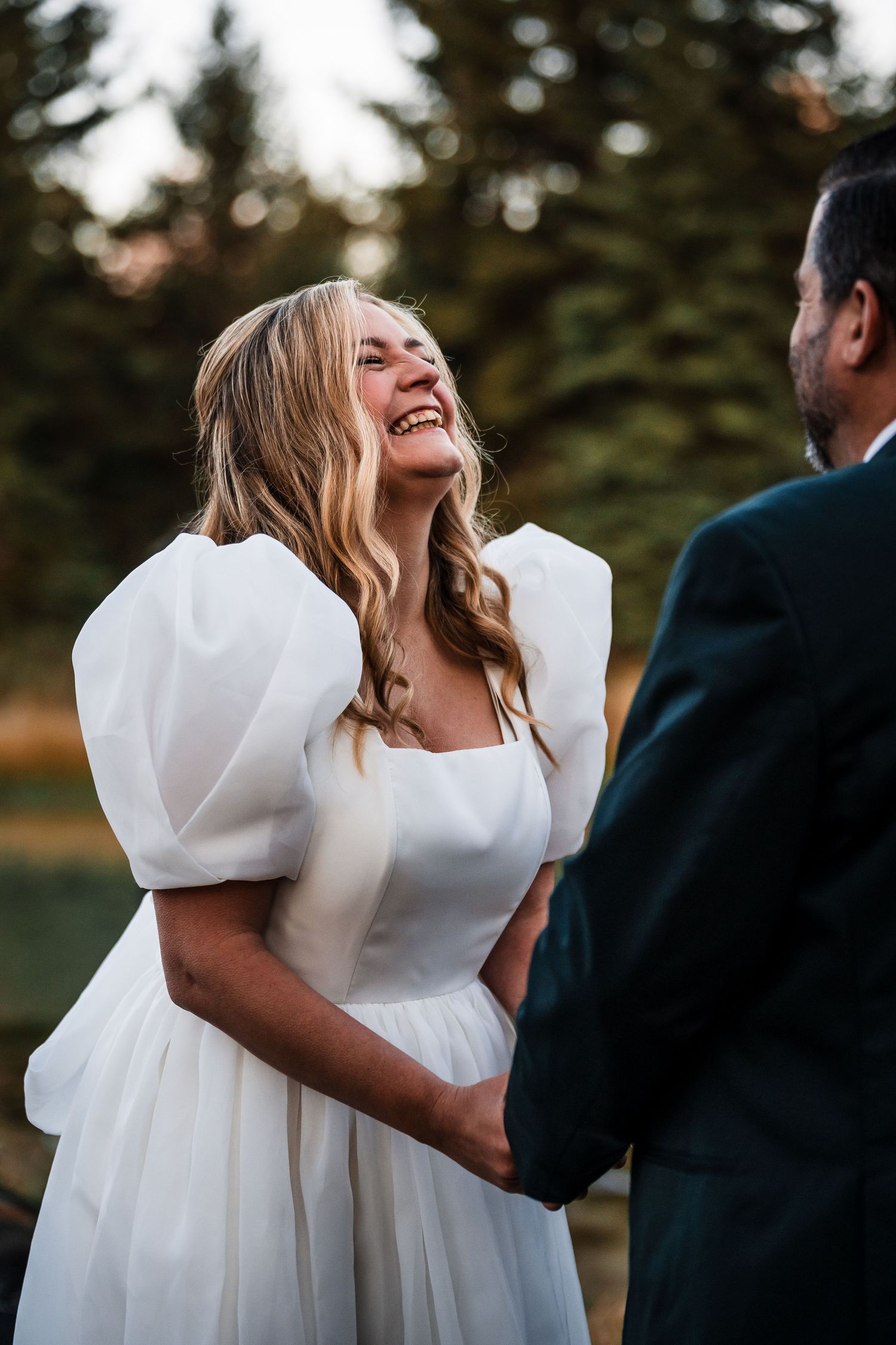 A couple shares a joyful moment during their wedding photoshoot in a natural outdoor setting.