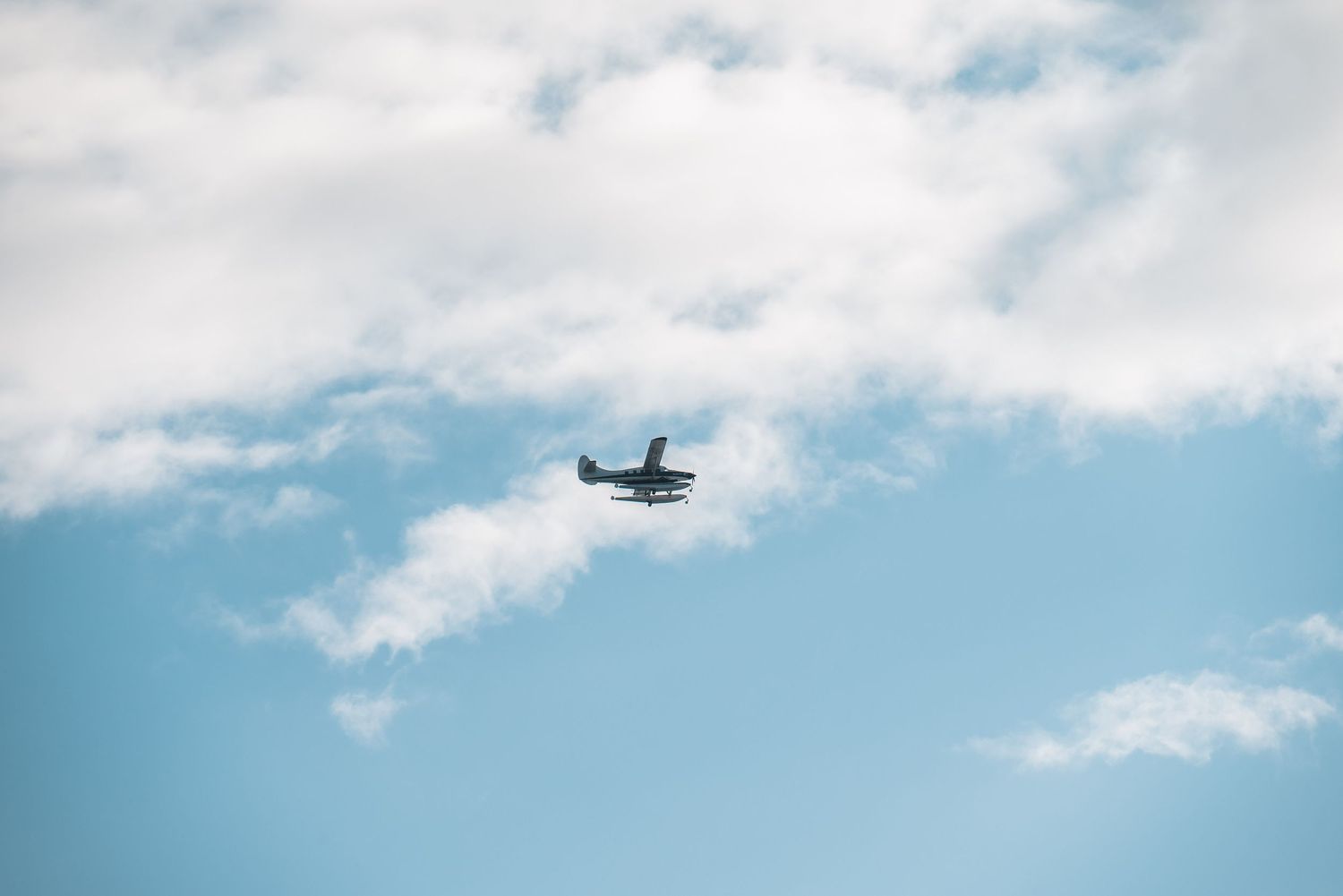 A small airplane flies through a bright blue sky with scattered white puffy clouds.