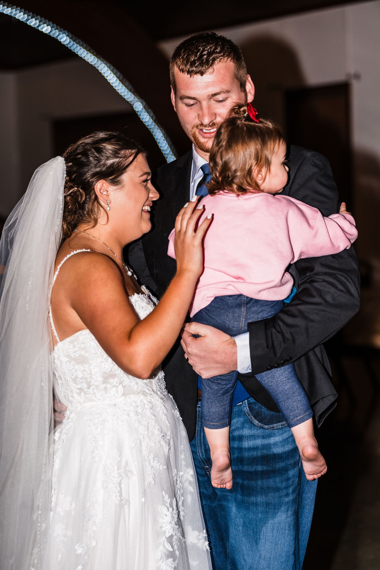 Wedding couple shares tender moment with small child in formal attire.