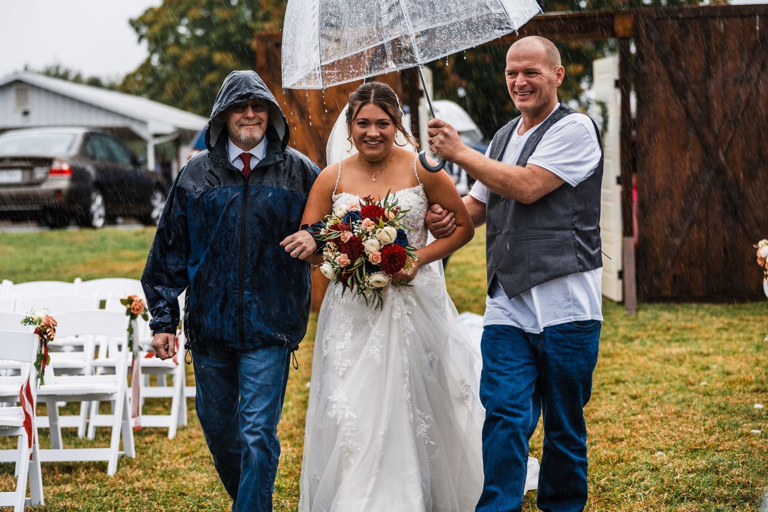 Wedding party members in denim and white attire celebrate on a grassy lawn with white chairs.