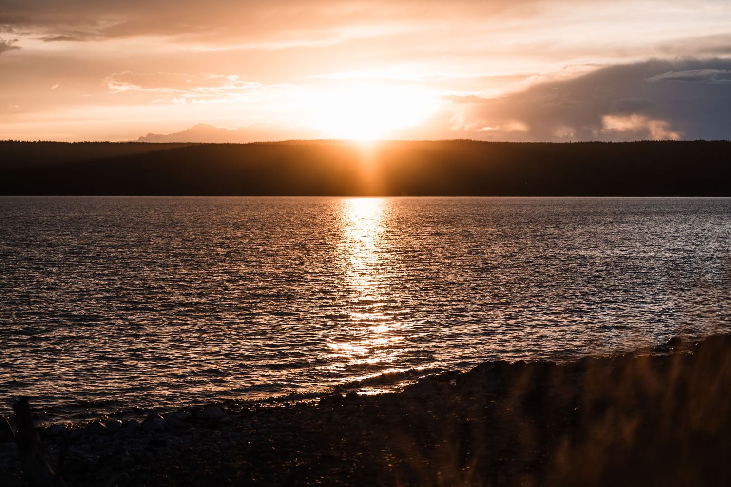 Vibrant orange sunset over a calm lake with silhouetted shoreline reflecting on the water.