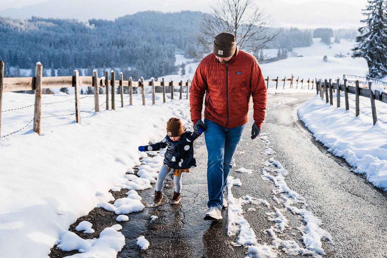 A winter walk along a snowy mountain path with a child and adult enjoying the scenic views together.