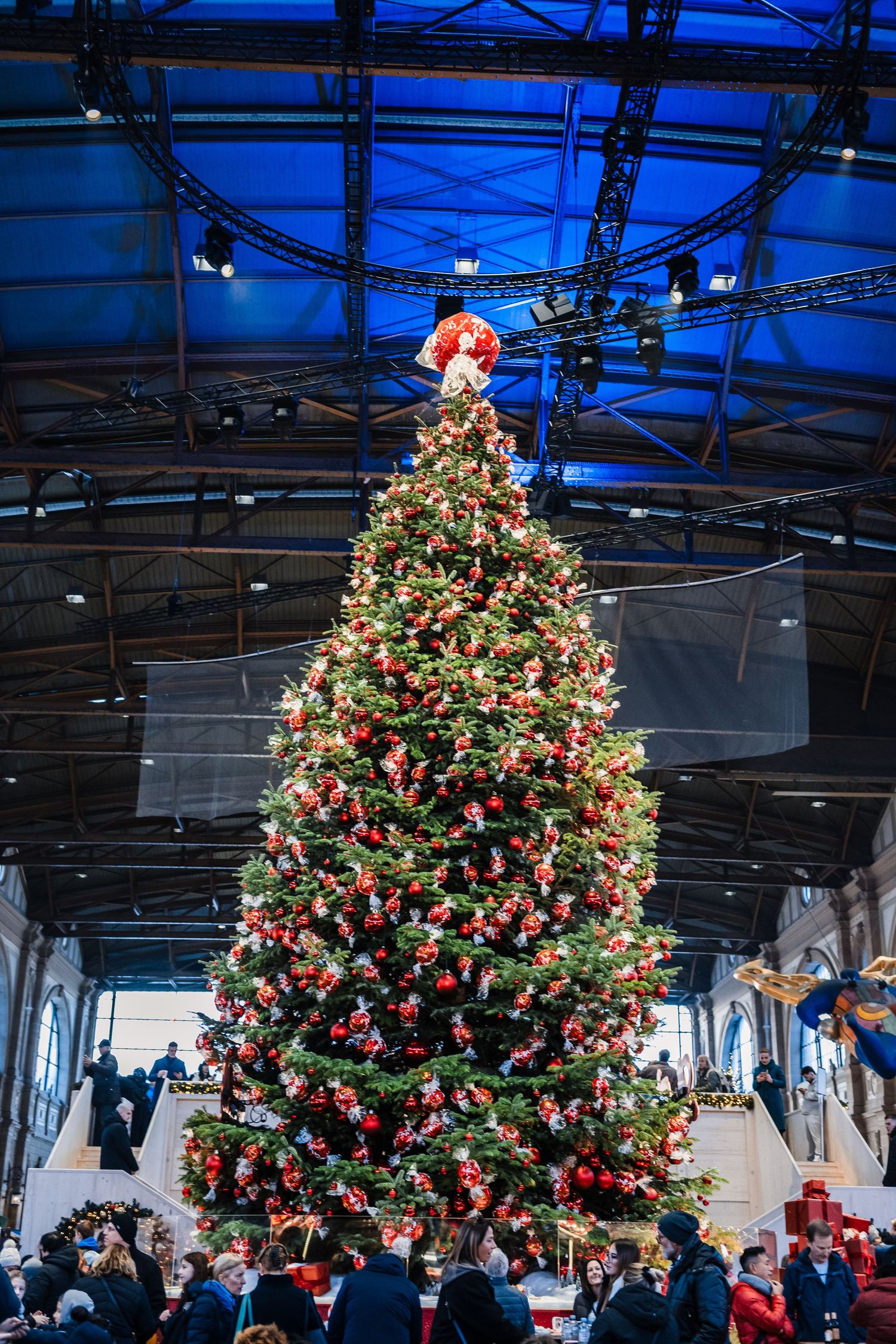 A sequence of photos showing a large decorated Christmas tree in a modern indoor venue with red and gold ornaments.