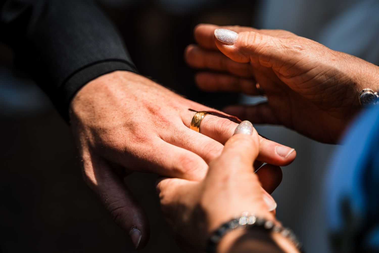 Close-up details of hands and wedding rings during an outdoor ceremony.