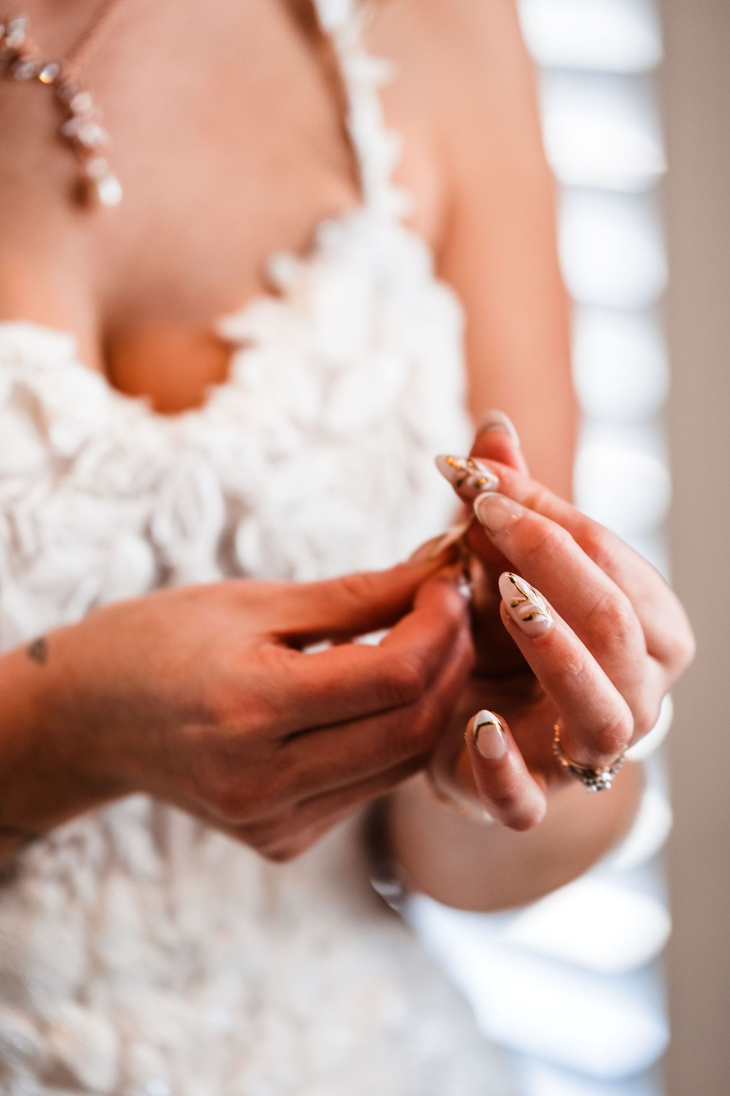 Elegant close-up shots of hands wearing wedding rings against a white lace dress background.