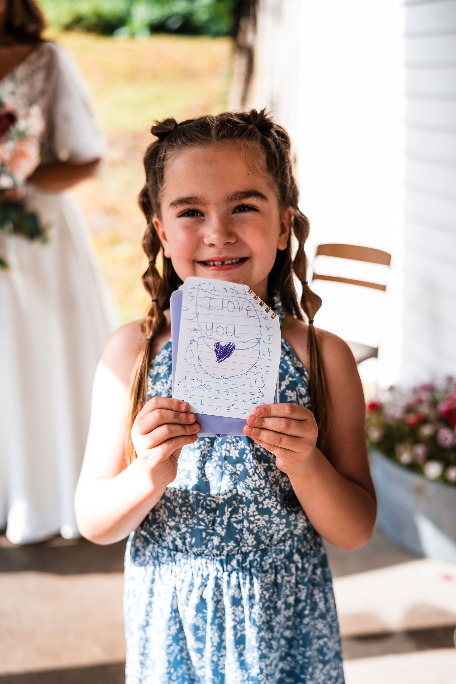 Young girl in floral dress excitedly holding up handwritten notes at a wedding.