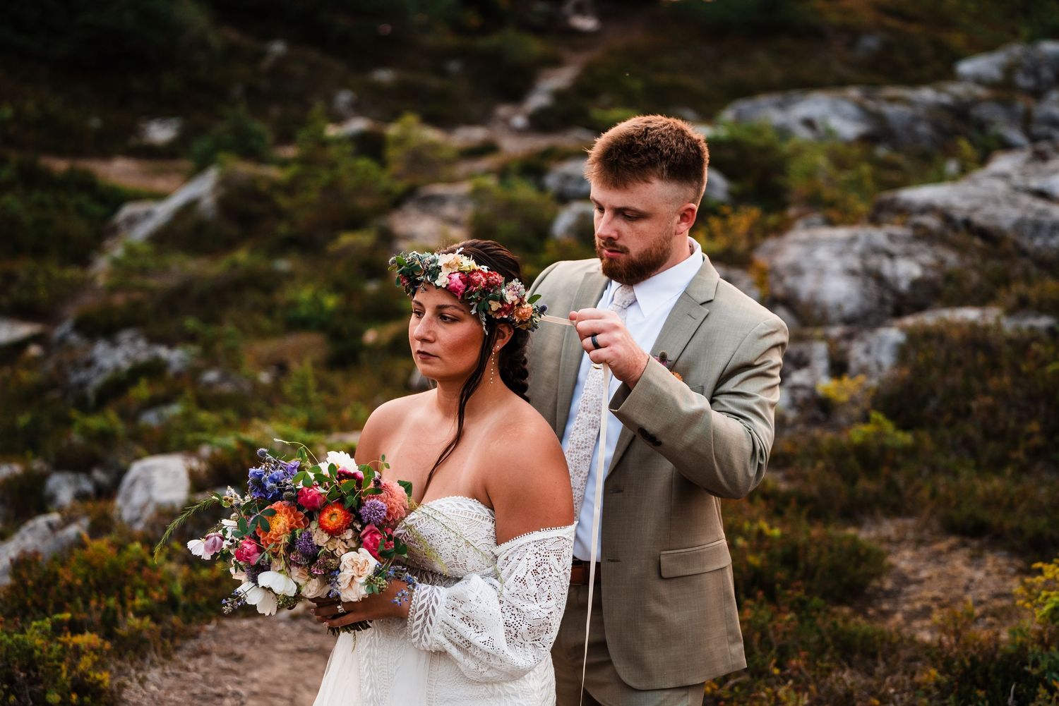 Couple shares intimate moment on rocky mountain terrain with wildflowers.