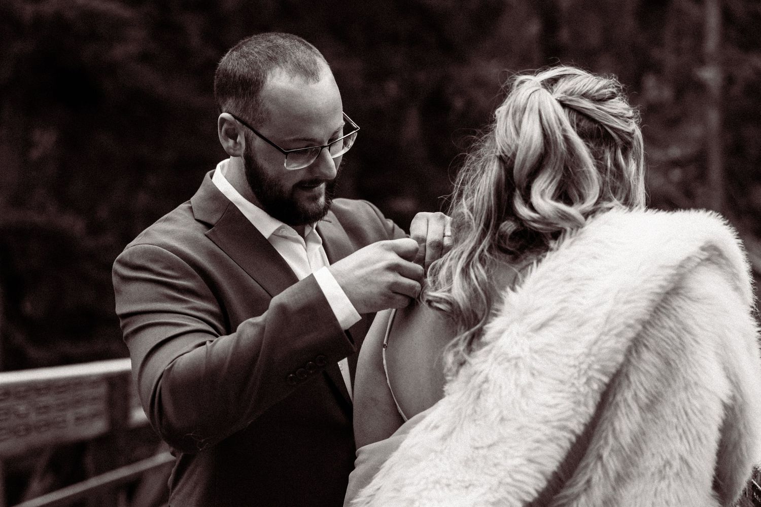 A couple shares a tender moment during their wedding day while posing with a white horse in a rustic outdoor setting.